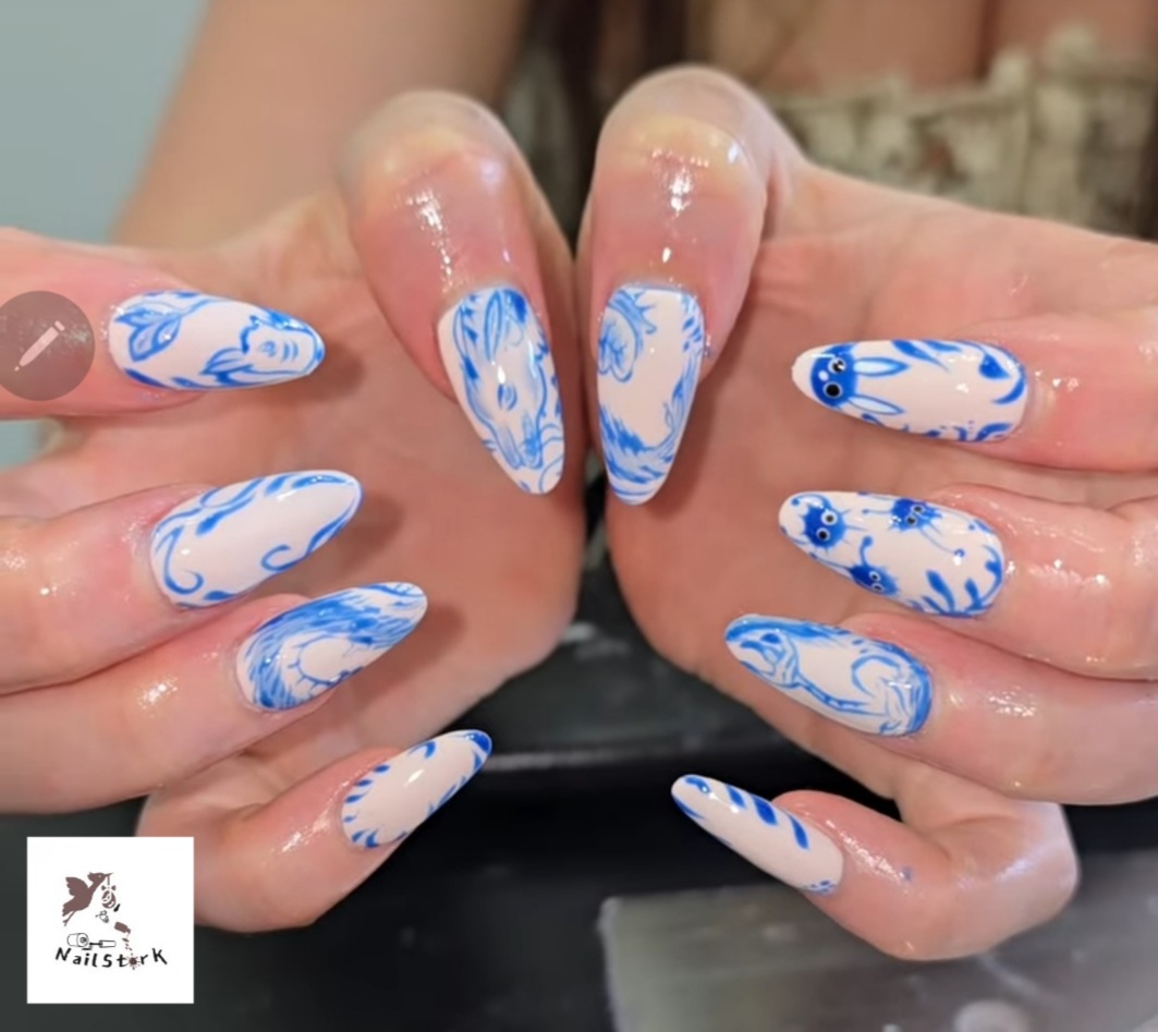Close-up of hands with decorated nails featuring blue floral and swirl designs on a white background.