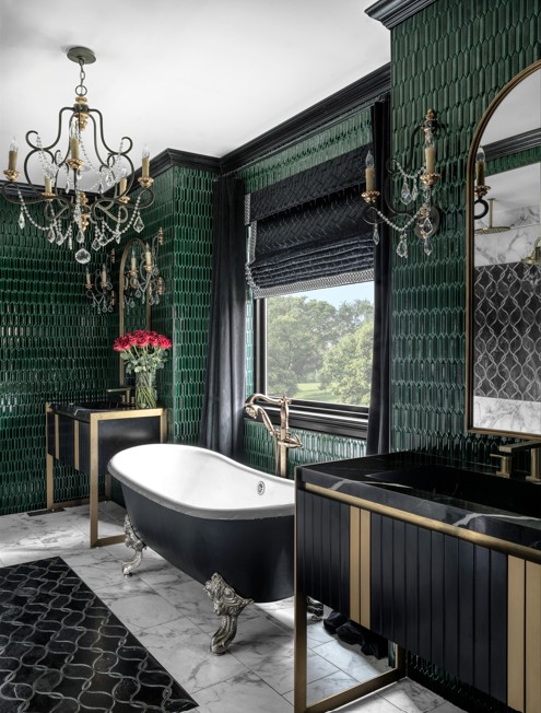 Luxurious bathroom with green tiled walls, clawfoot bathtub, black and gold vanity, chandelier, and window with view outside.