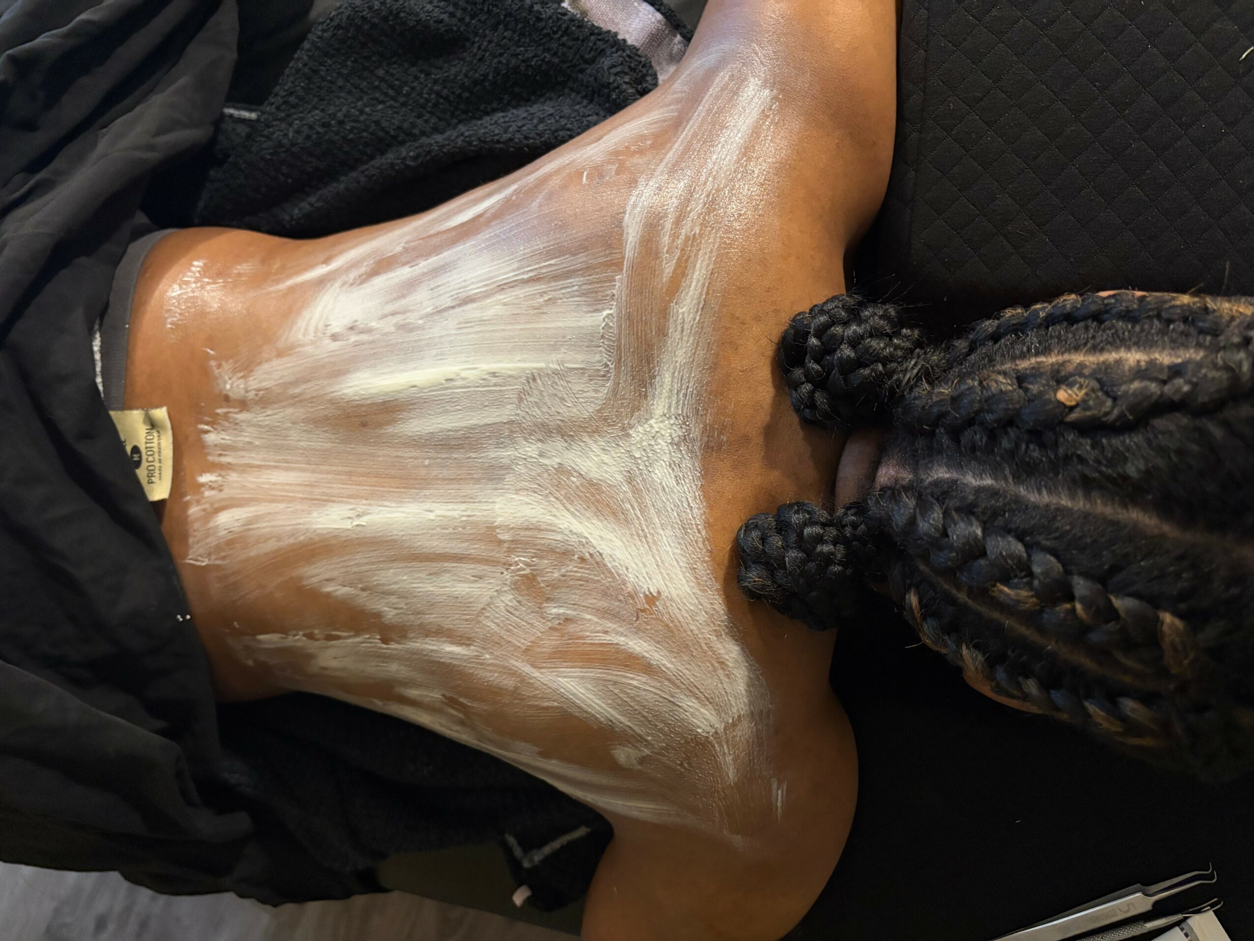 Person lying down with braided hair, covered in a white substance on their chest and neck area.