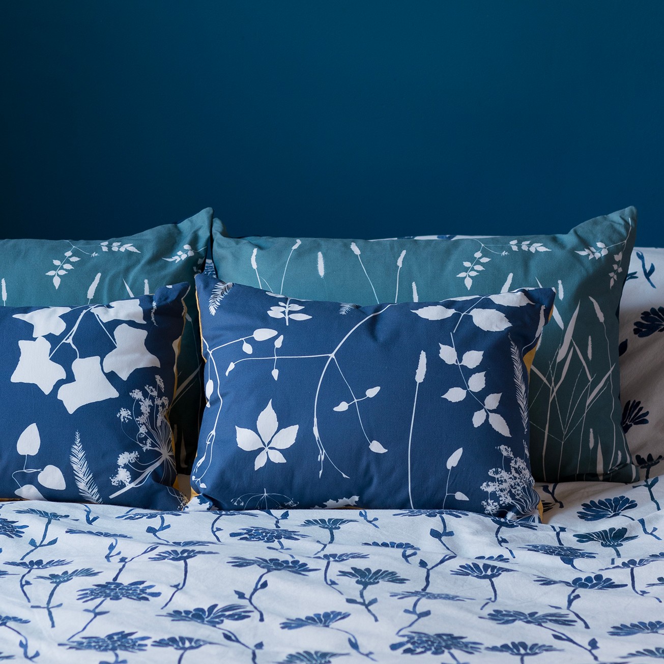 Close-up of decorative pillows with blue and white floral patterns on a bed, with a blue wall in the background.