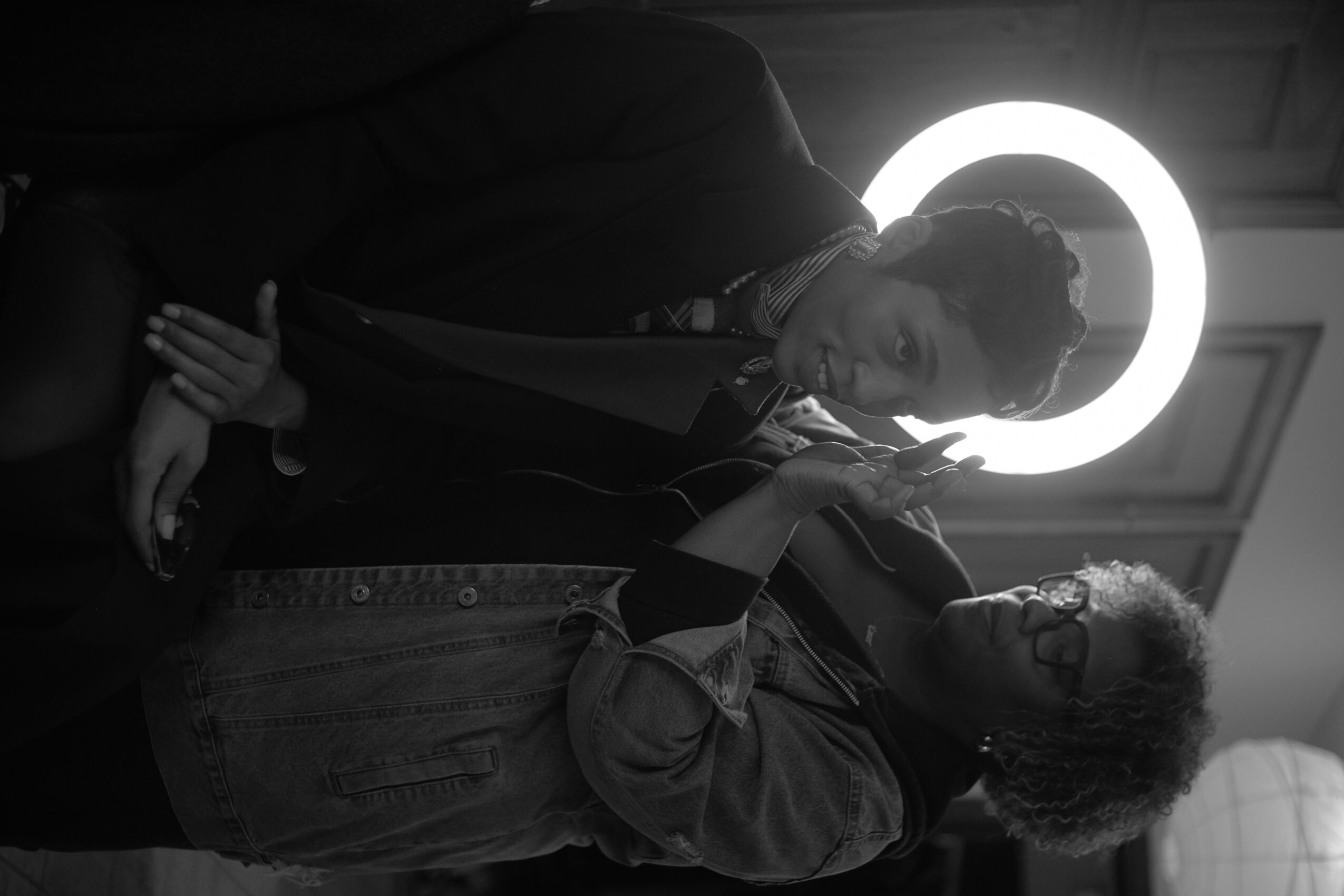 Two people standing in front of a circular light, one with glasses and curly hair, the other with straight hair and a ring.