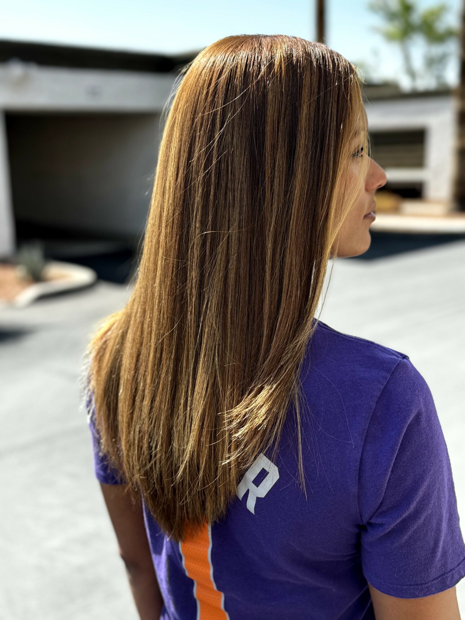 Side view of a woman with long, straight, light brown hair wearing a purple shirt outdoors.