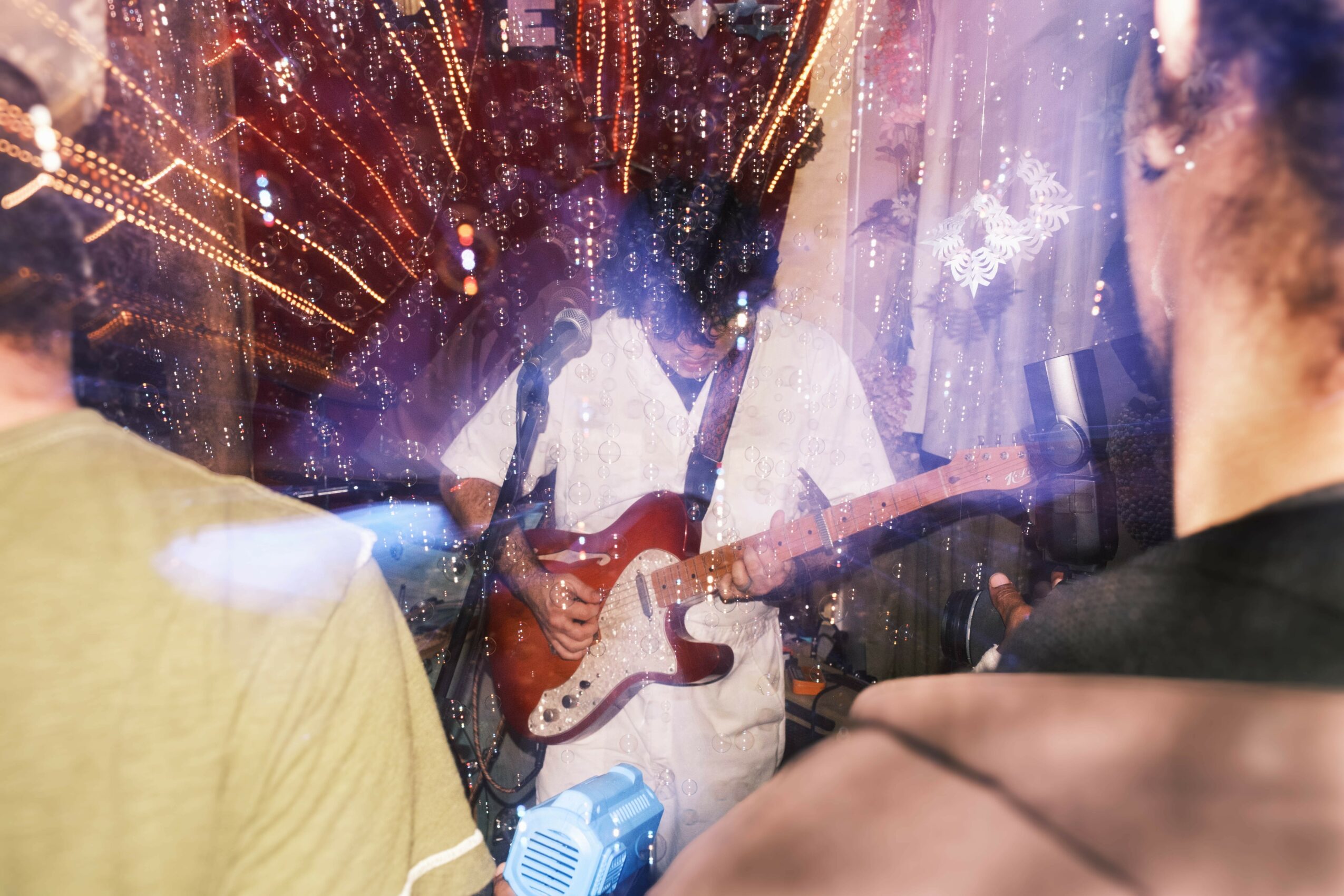 People watching a musician playing guitar through a glass window with colorful lights and reflections, creating a vibrant scene.