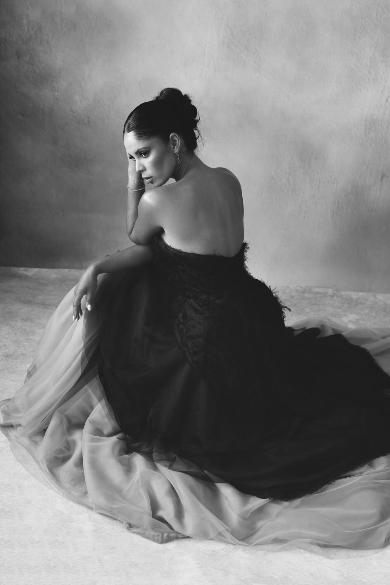 Woman sitting on the floor with her back partially turned, wearing a strapless dress, in black and white.