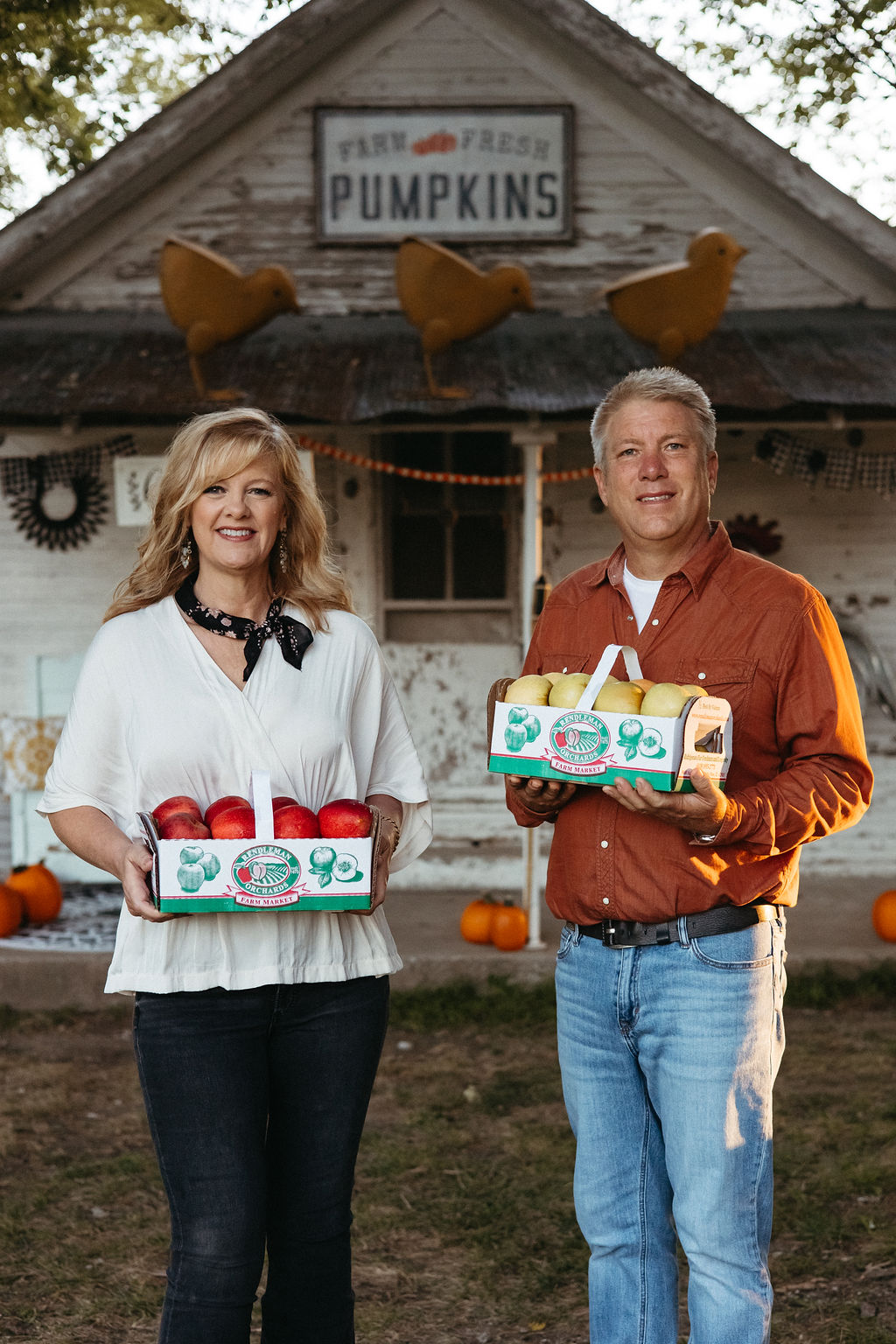 A woman and a man holding pumpkin boxes stand in front of a house with a pumpkin sign and decorations.