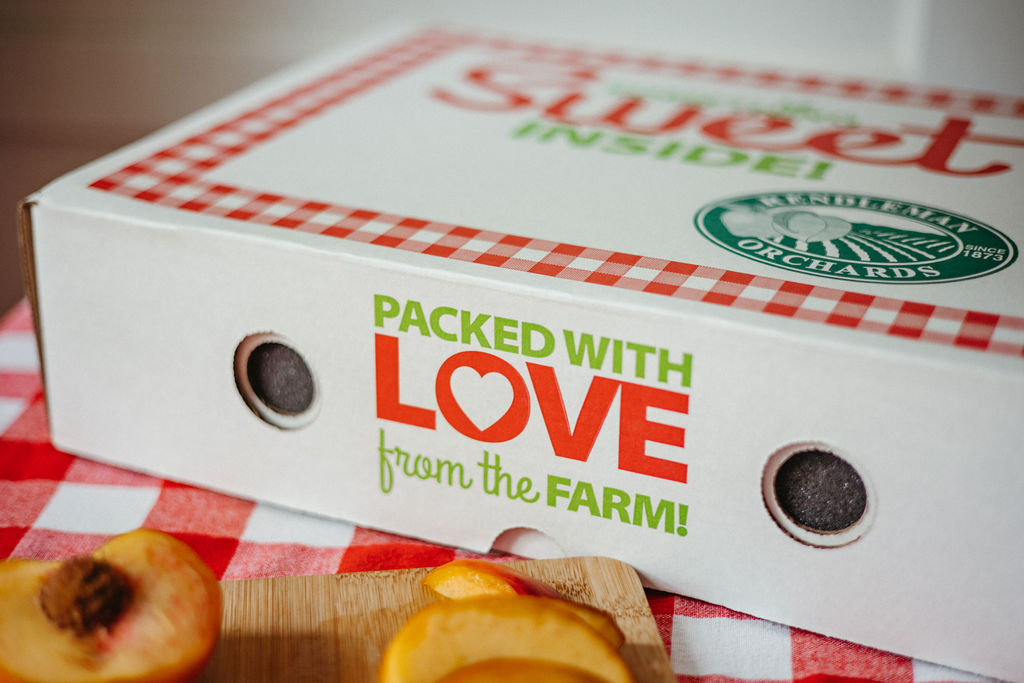 Close-up of a pizza box with a sticker that says 'Packed with Love from the Farm!' on a checkered tablecloth.