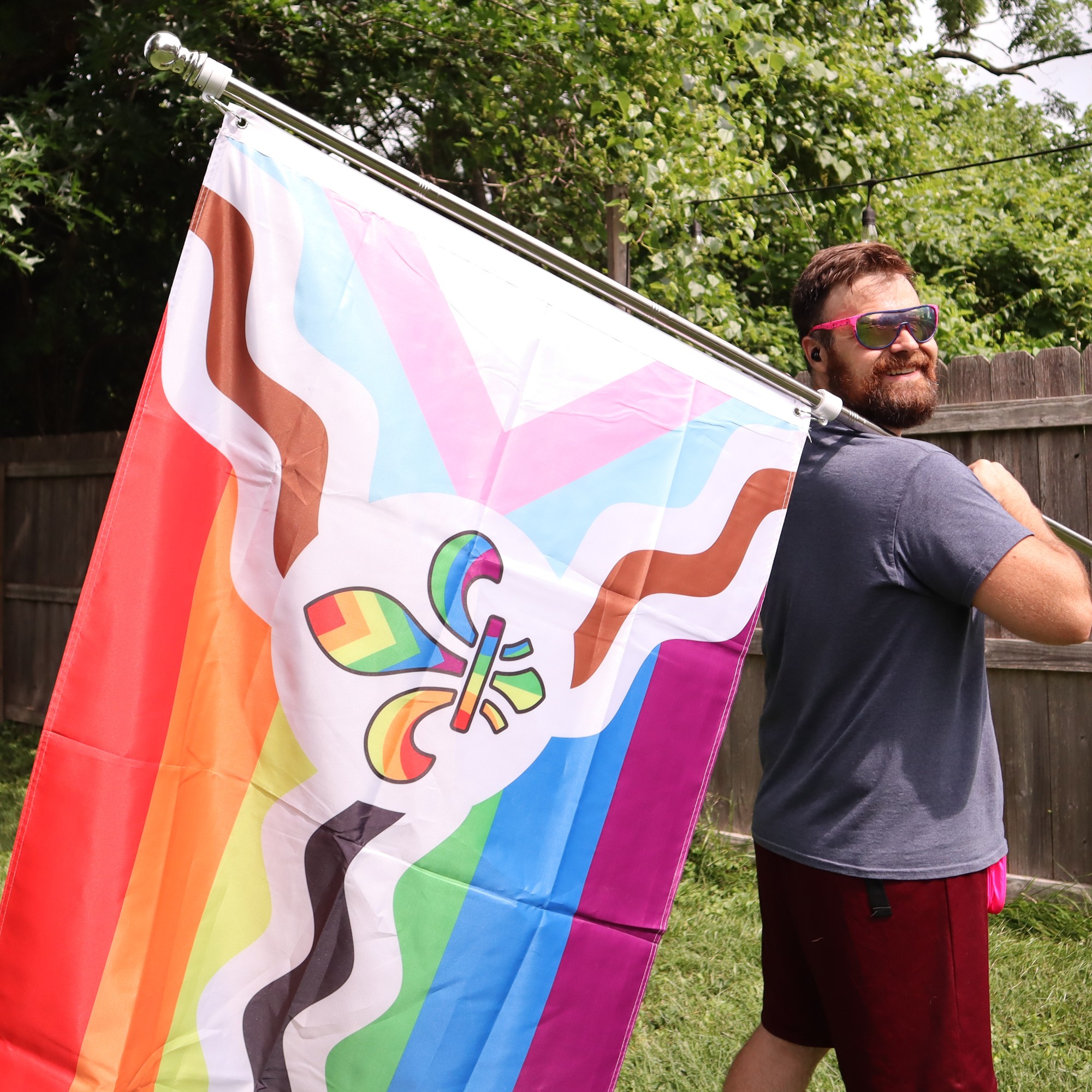 Person holding a rainbow flag with a butterfly design outdoors, with trees and a wooden fence in the background.