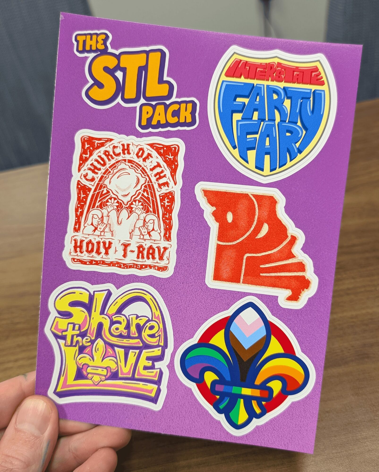 Purple sheet with six colorful stickers, including text and various designs, held by a person's hand.