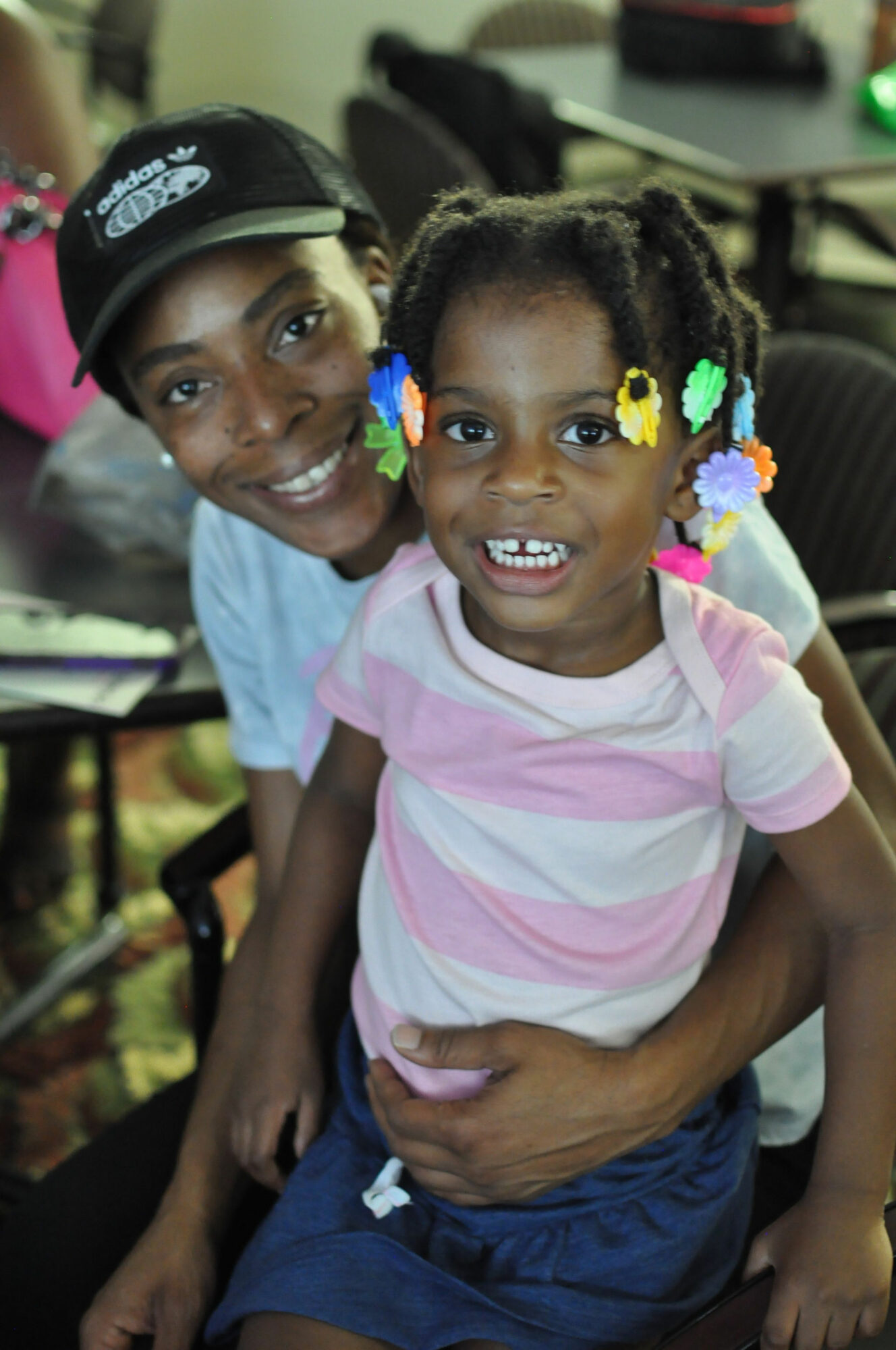 Two children smiling, one with colorful hair beads, in a classroom setting.