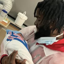 Person holding a newborn baby in a hospital room, with medical supplies in the background.