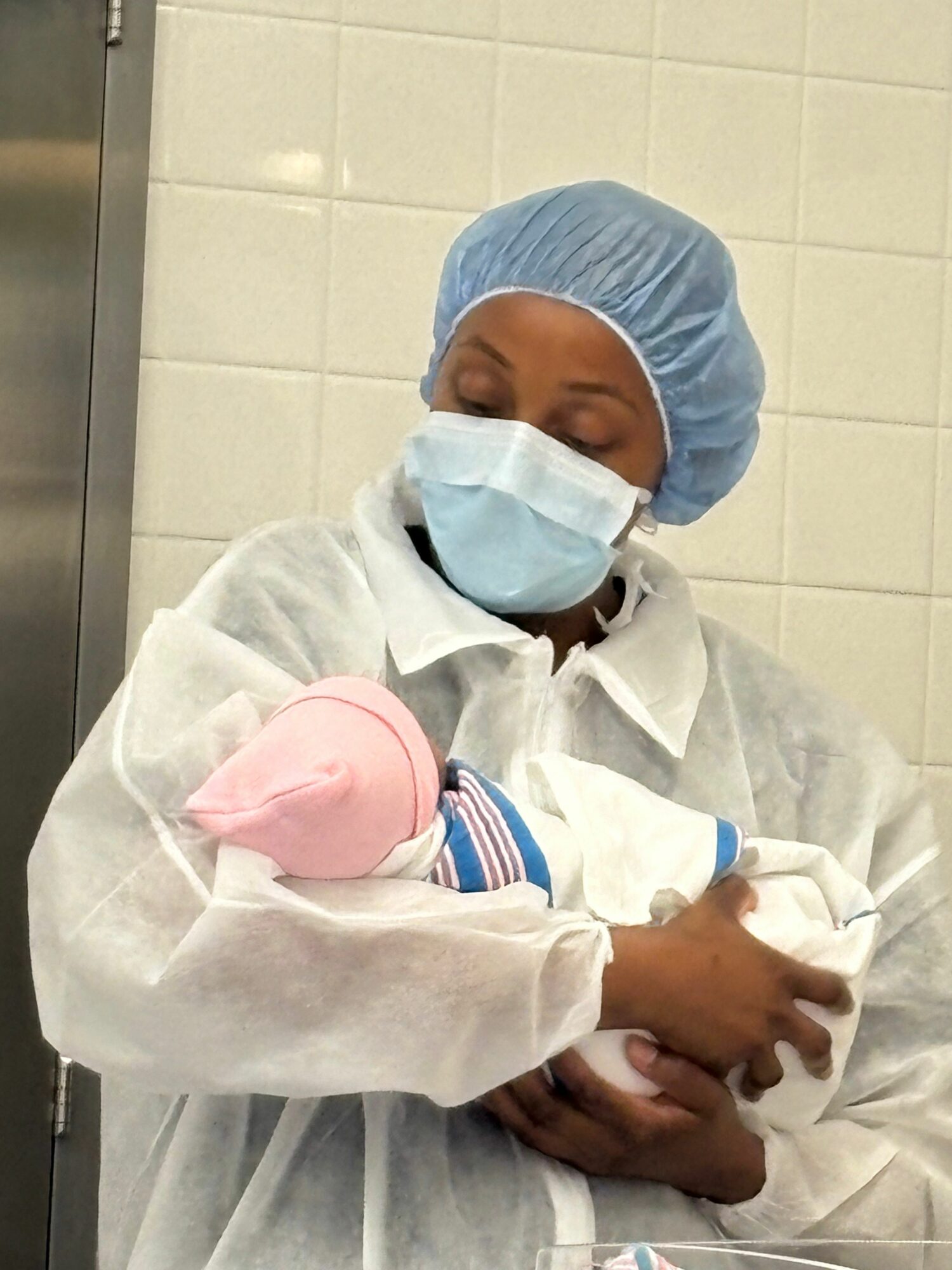 Healthcare worker in protective gear, including mask, gown, and cap, holding a child's hand in a clinical setting.