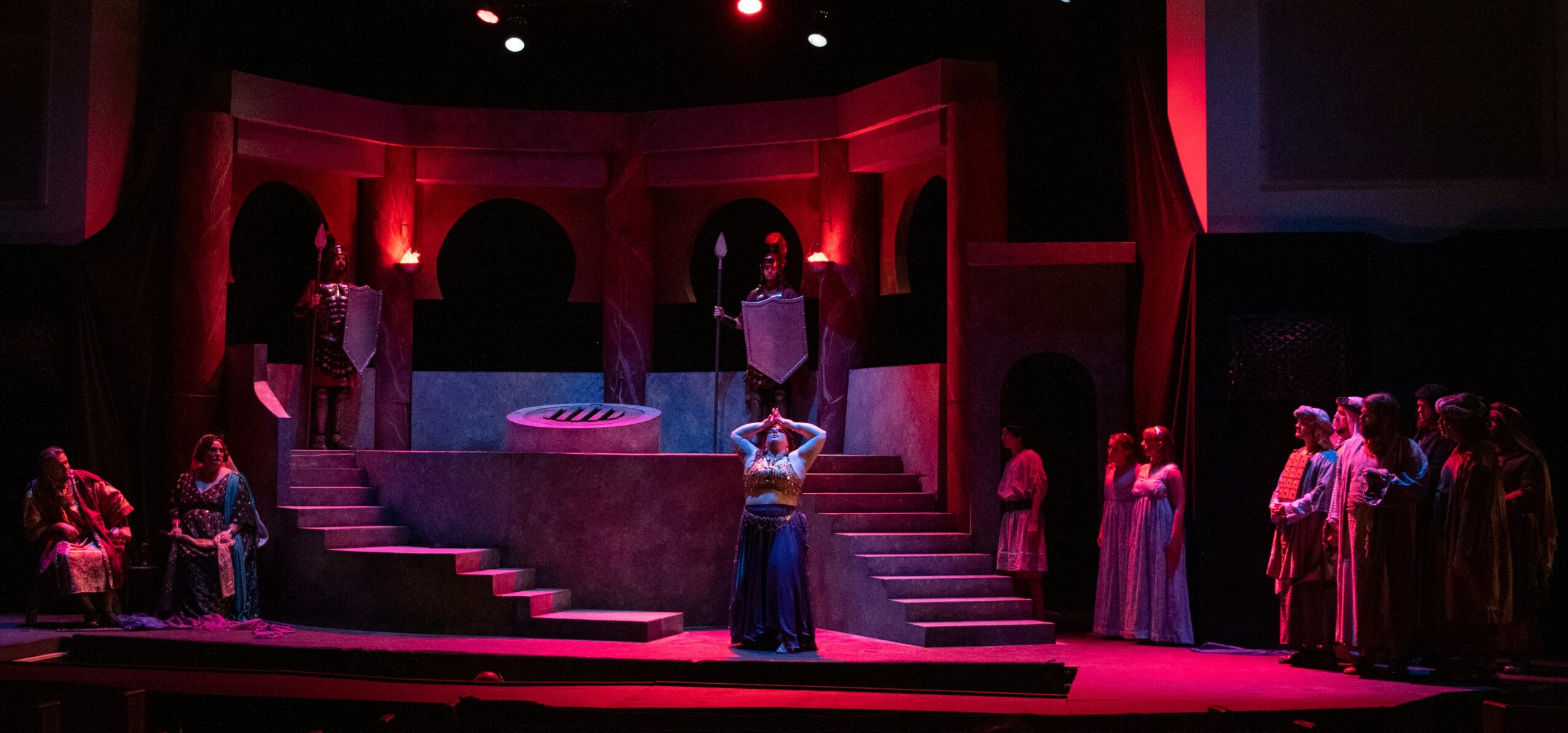 Stage with actors, stairs, and red lighting, set for a theatrical performance.