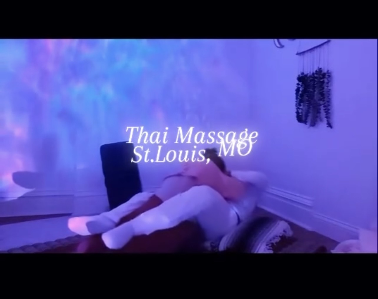 Two people lying on a massage table in a room with purple lighting, with text overlay about Thai massage in St. Louis.