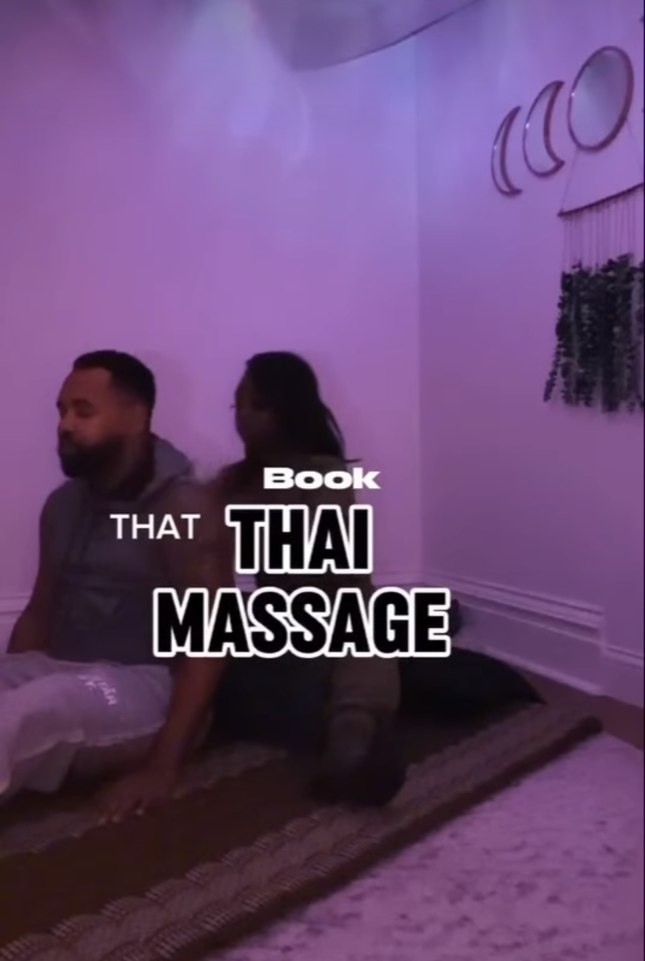 Two people sitting on a mat in a room with purple lighting, with text about Thai massage and a book, 20 words.