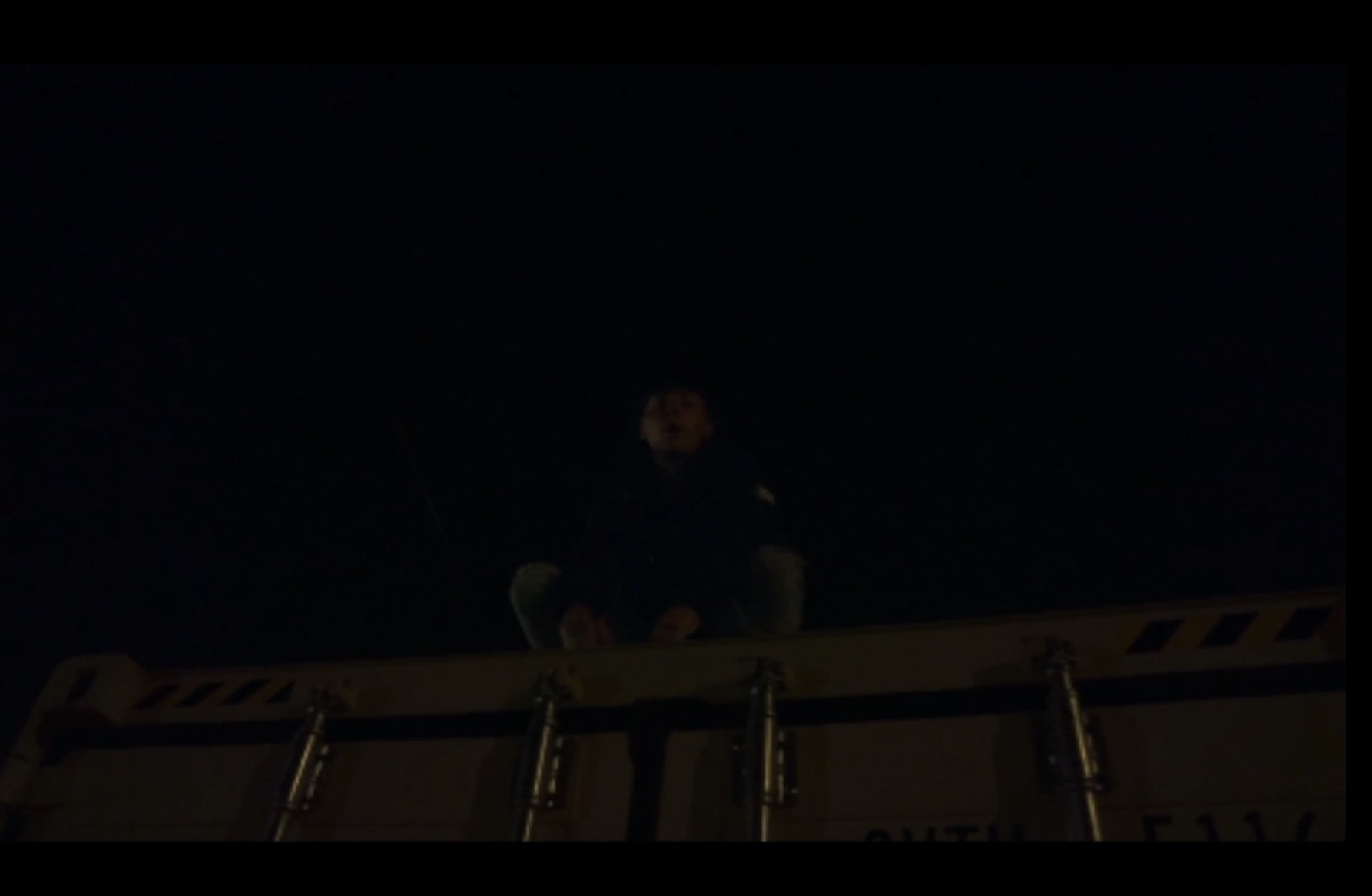 Person standing on a platform at night, with a dark sky background.