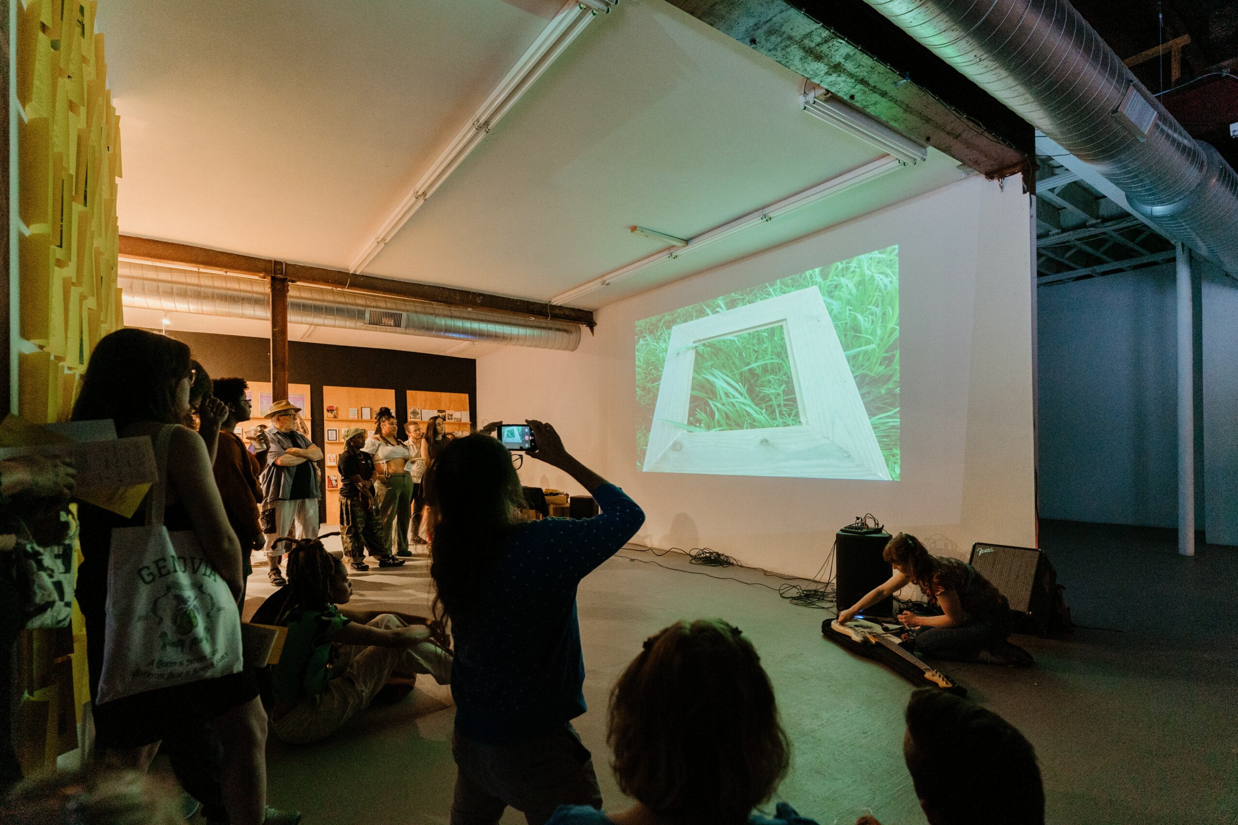 People watching a presentation projected on a large white wall in an industrial-style room.