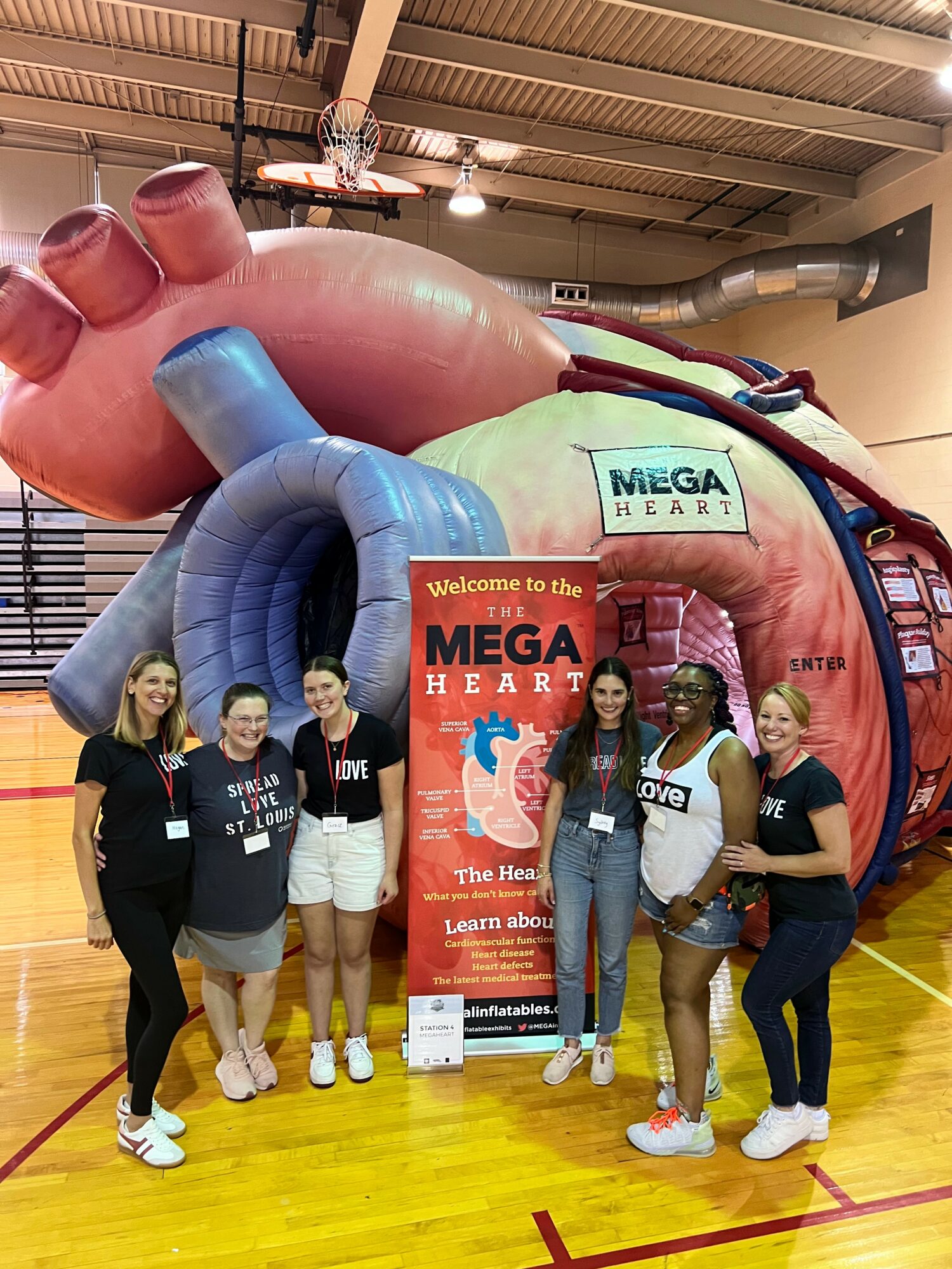 Four people stand in front of a large inflatable heart structure with a sign that reads