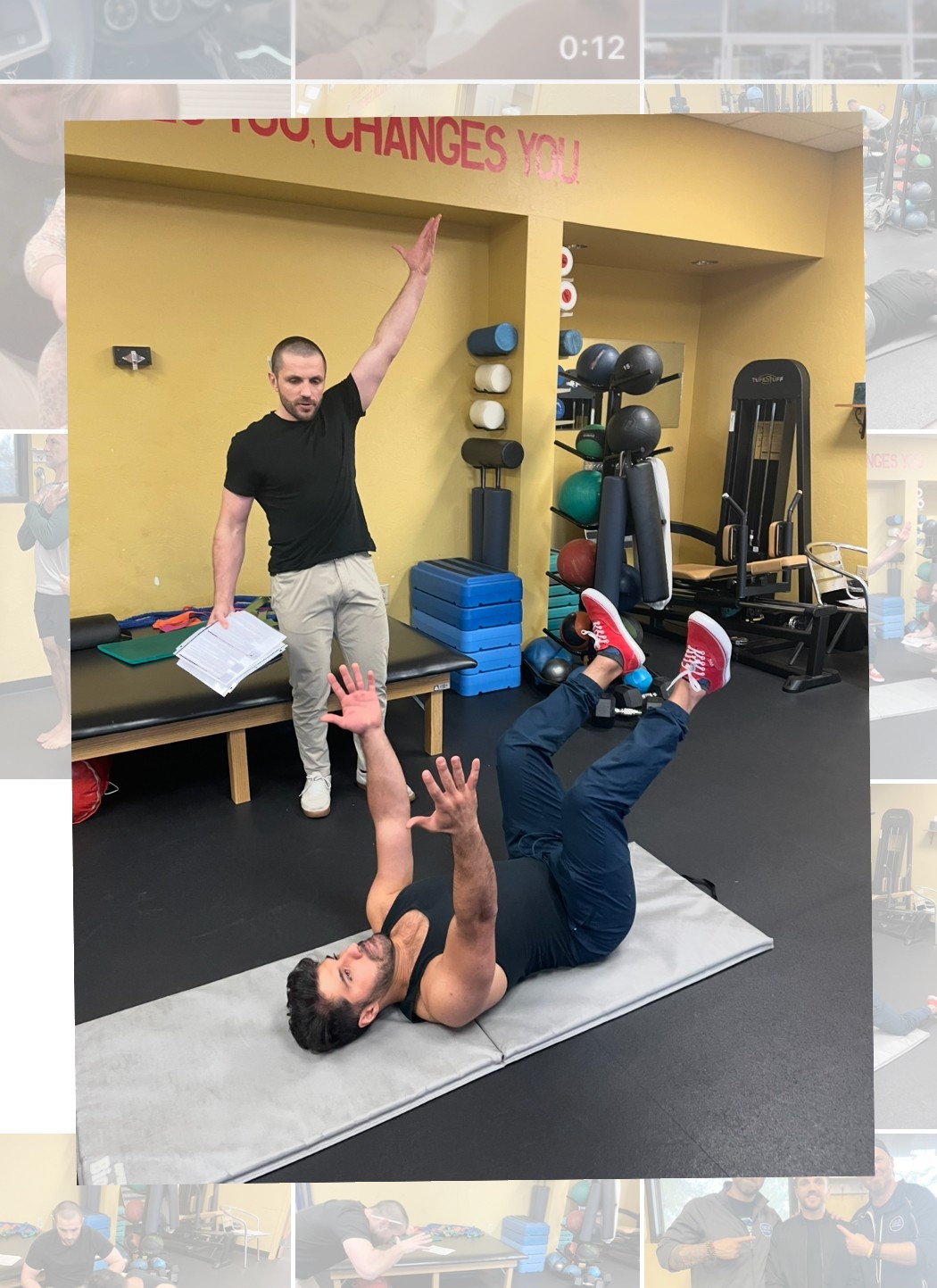 Two people in a gym, one lying on a mat with arms raised, the other standing with one arm raised, gym equipment in background.
