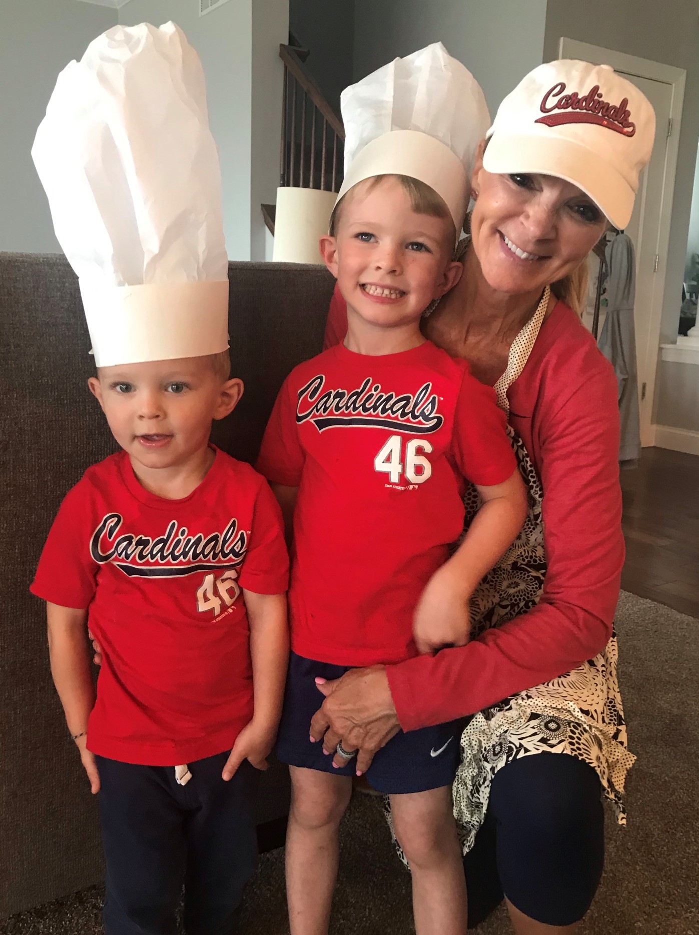 Woman and two children wearing red Cardinals shirts, one child with a chef's hat, smiling indoors.