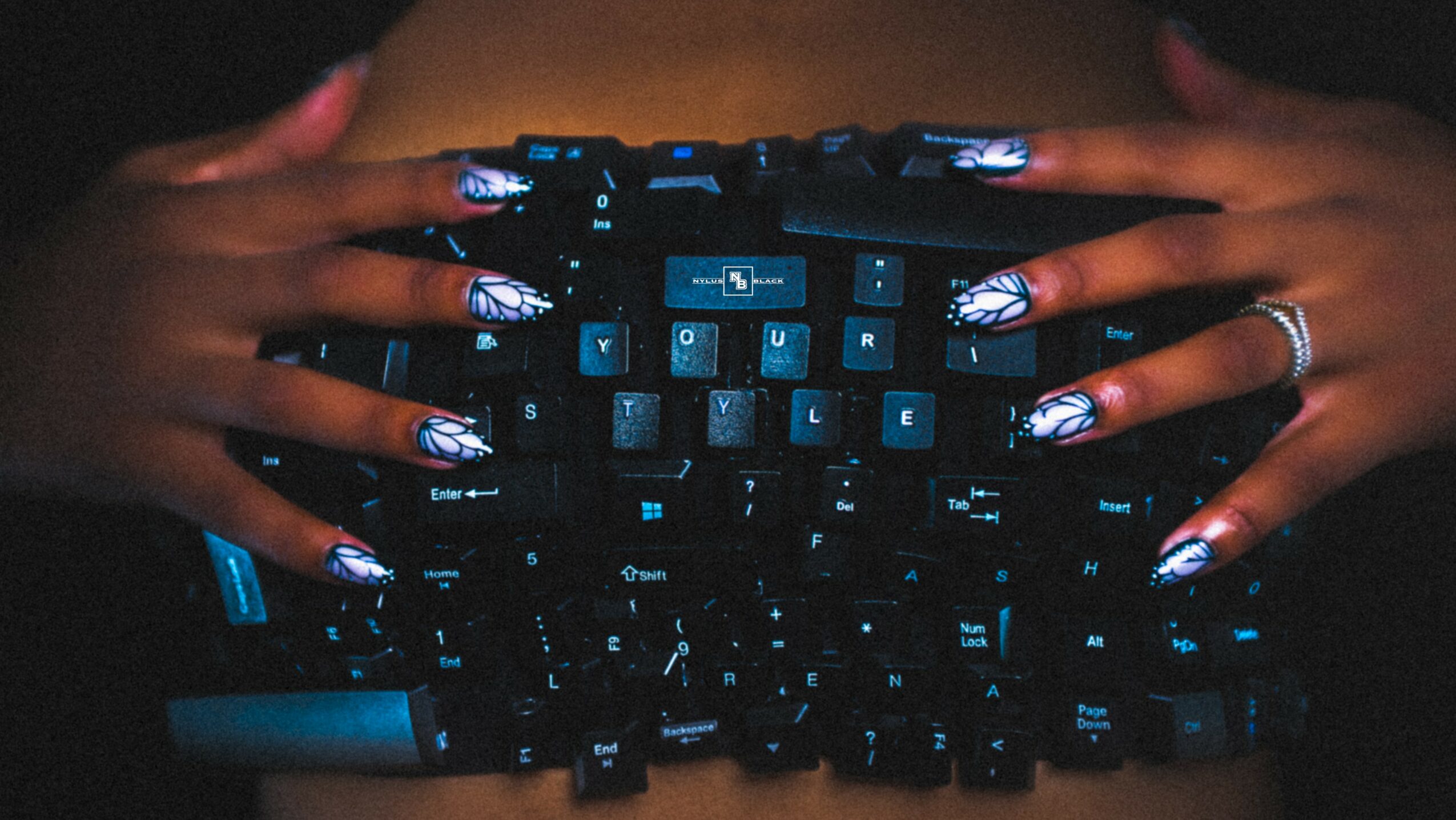 Hands with decorated nails holding a black computer keyboard in a dark setting.