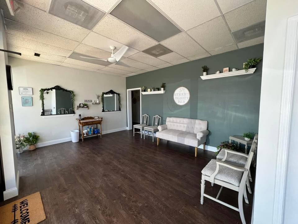 Room with dark wood floor, white and gray walls, two chairs, a sofa, and shelves with plants and decor.