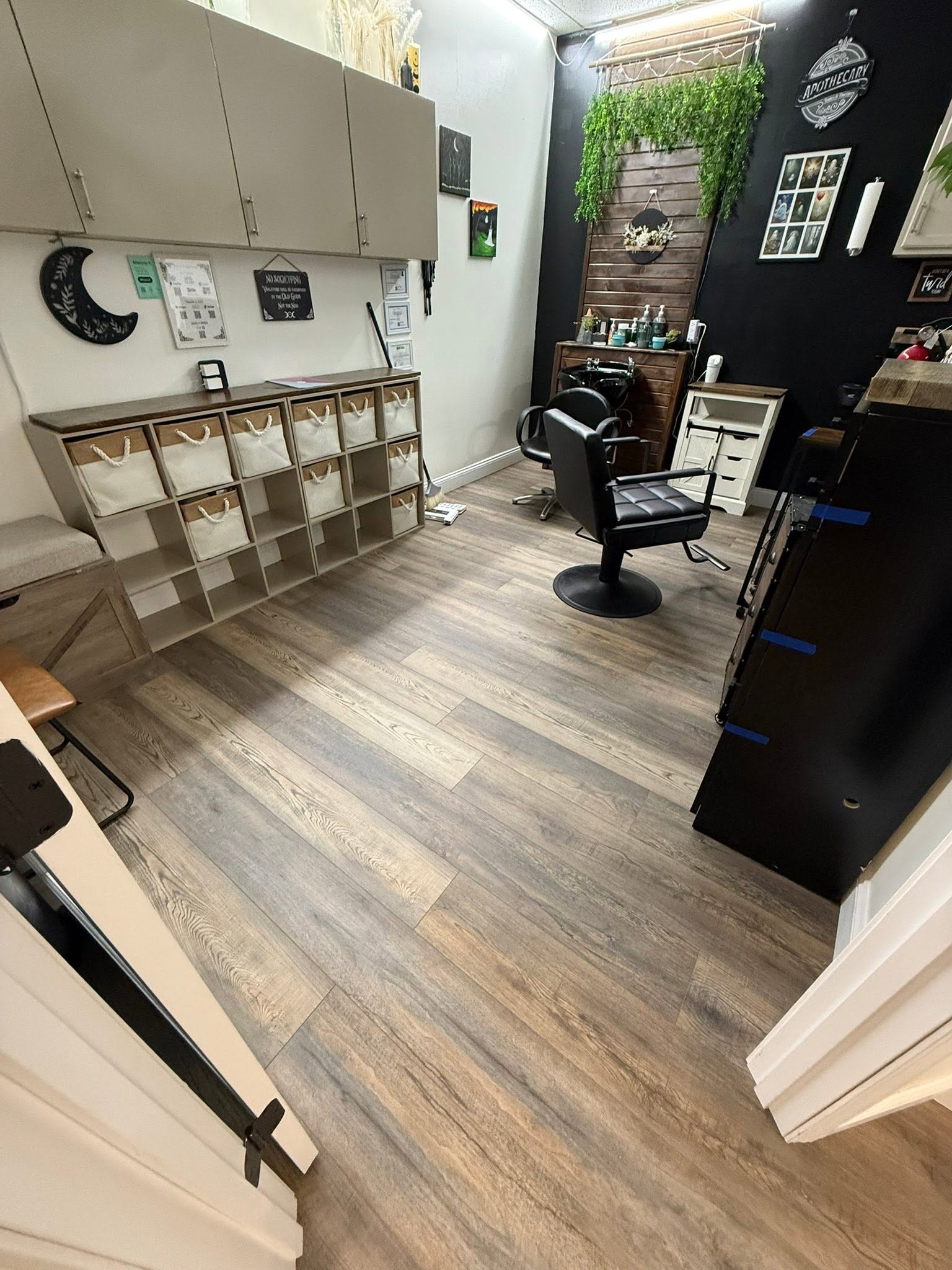 Office space with desk, chair, storage, and decorative wall elements, viewed from doorway. Wooden floor and wall decor visible.