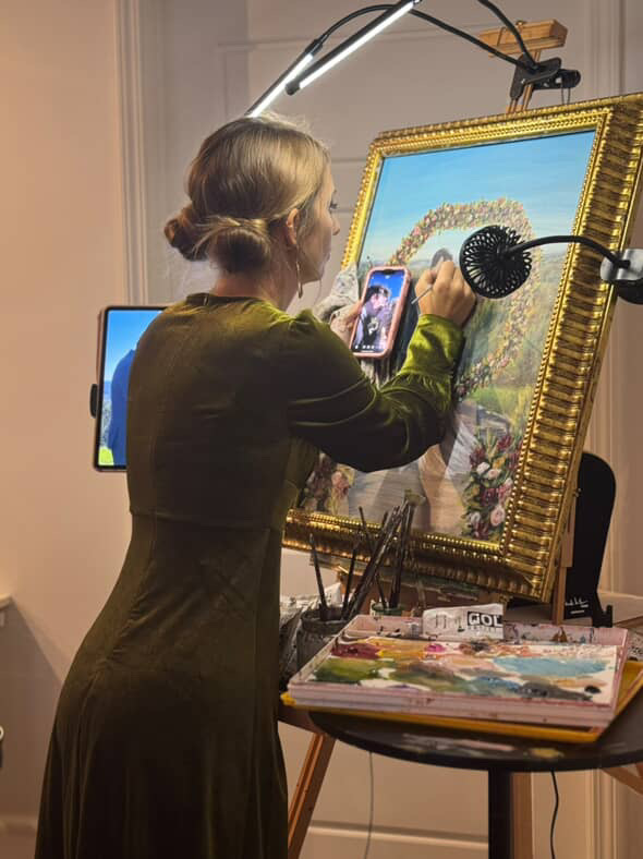 Woman painting on a large canvas, holding a palette, with a smartphone in her other hand, in an art studio.