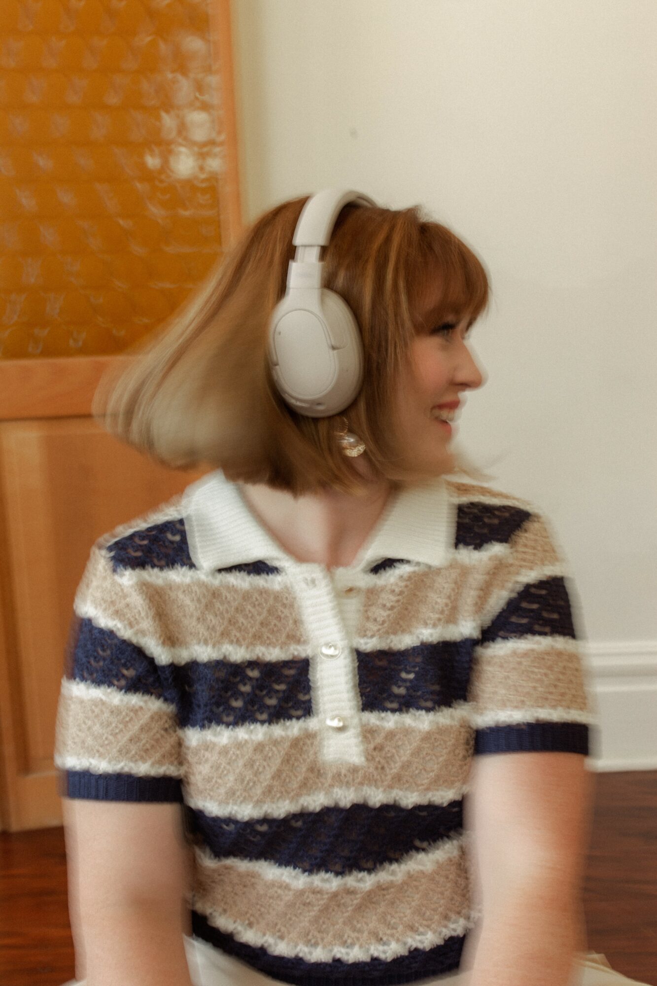 Side profile of a woman with shoulder-length hair wearing large white headphones and a striped shirt.