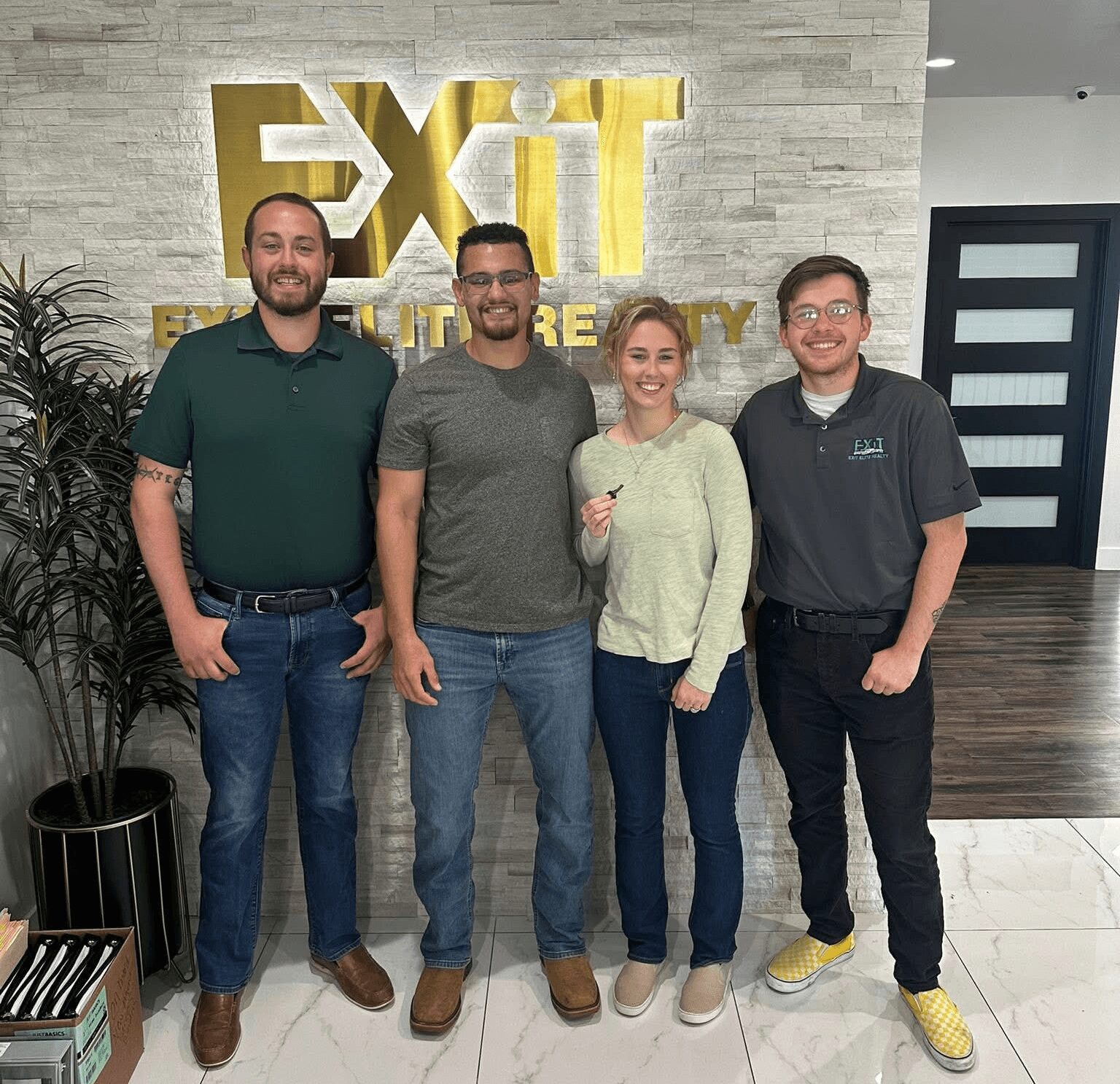 Four people standing in front of a wall with a large gold sign that says 'EXIT'.