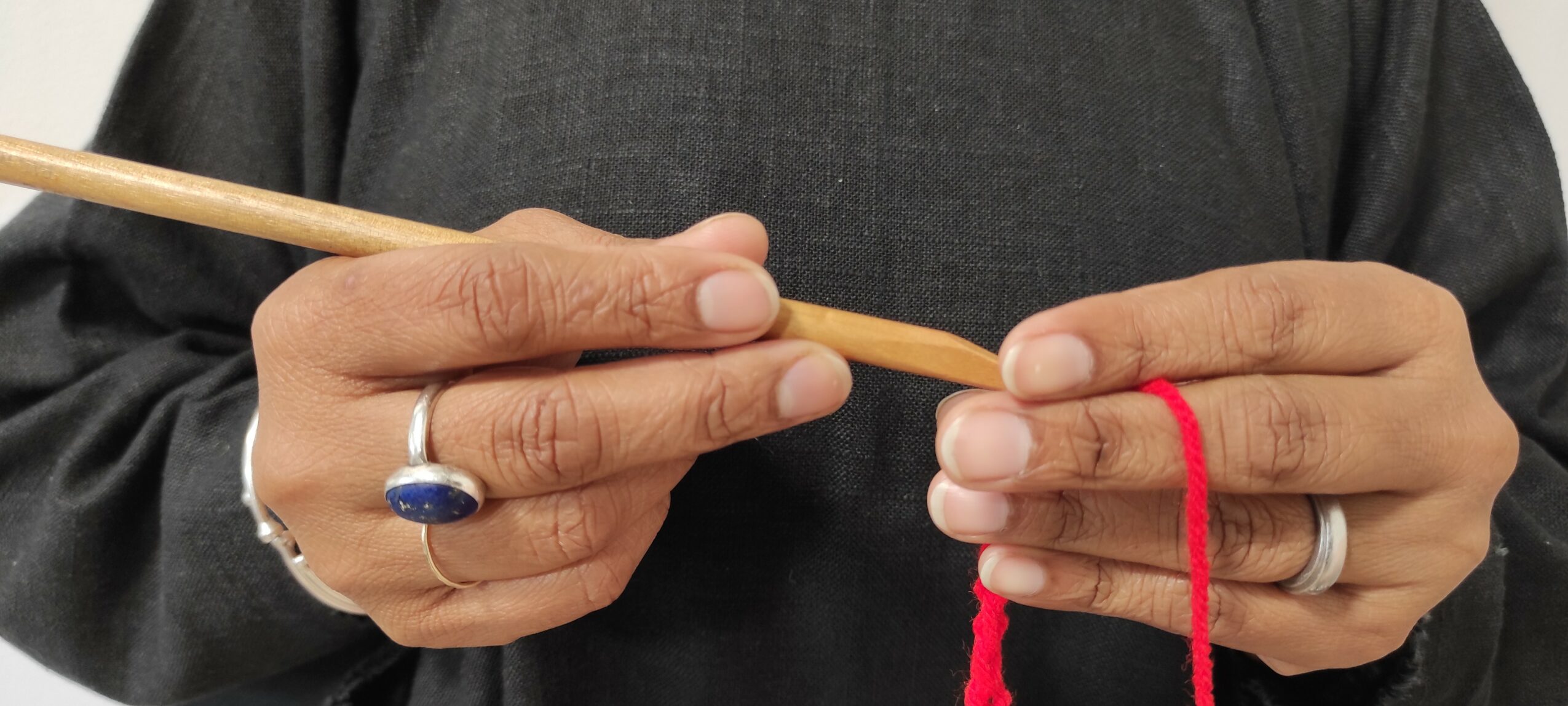 Person holding a wooden stick with red thread, wearing rings, dark clothing.