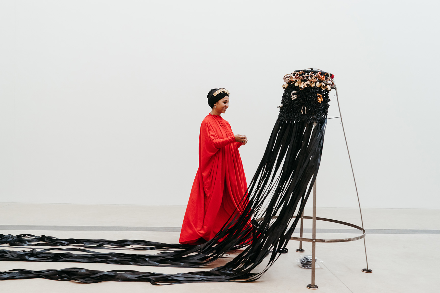 Woman in red dress looking at an art installation with black ribbons and flowers, in a gallery space.
