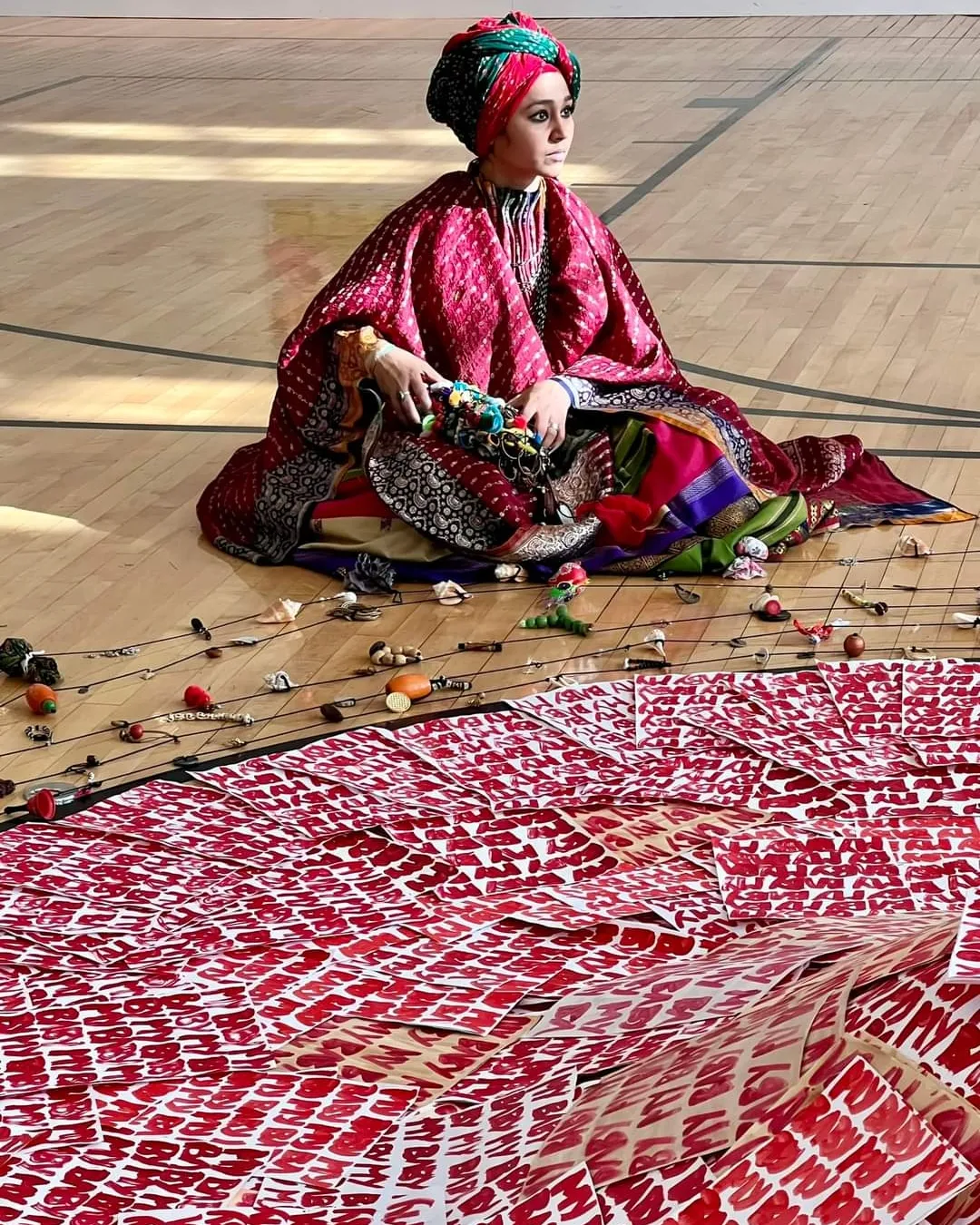 Person dressed in traditional attire sitting on a wooden floor with scattered flowers and a patterned cloth in front.