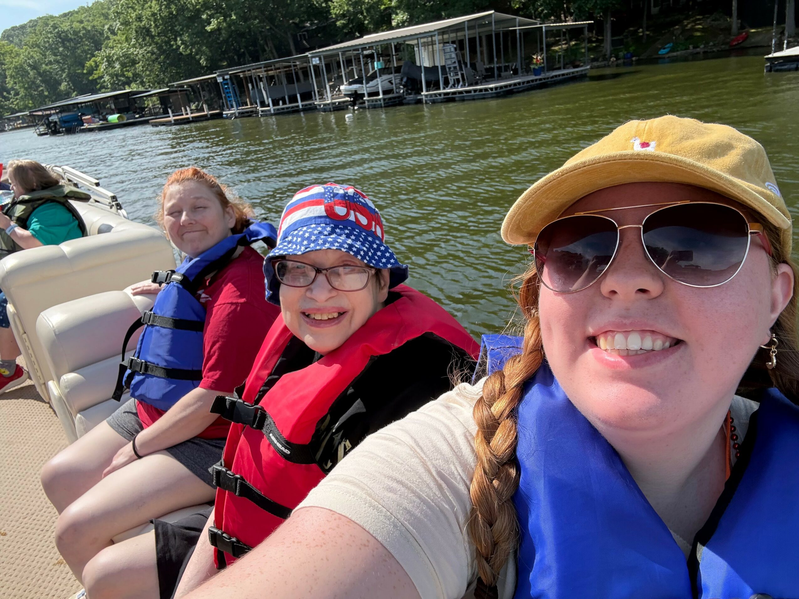 Three children on a boat wearing life jackets, smiling, with a waterway and docks in the background.