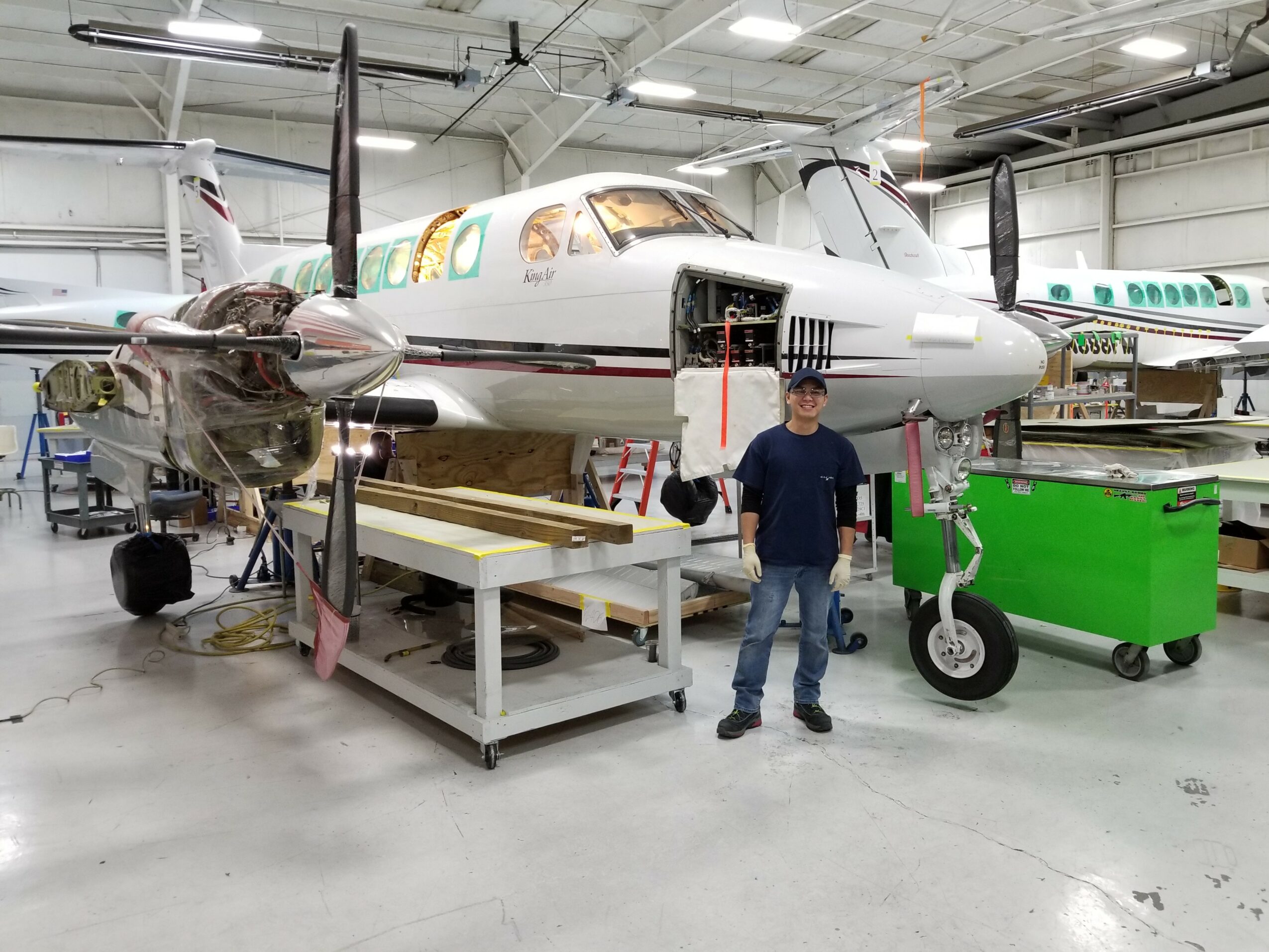 Person standing next to a small aircraft inside a hangar, with maintenance equipment nearby.
