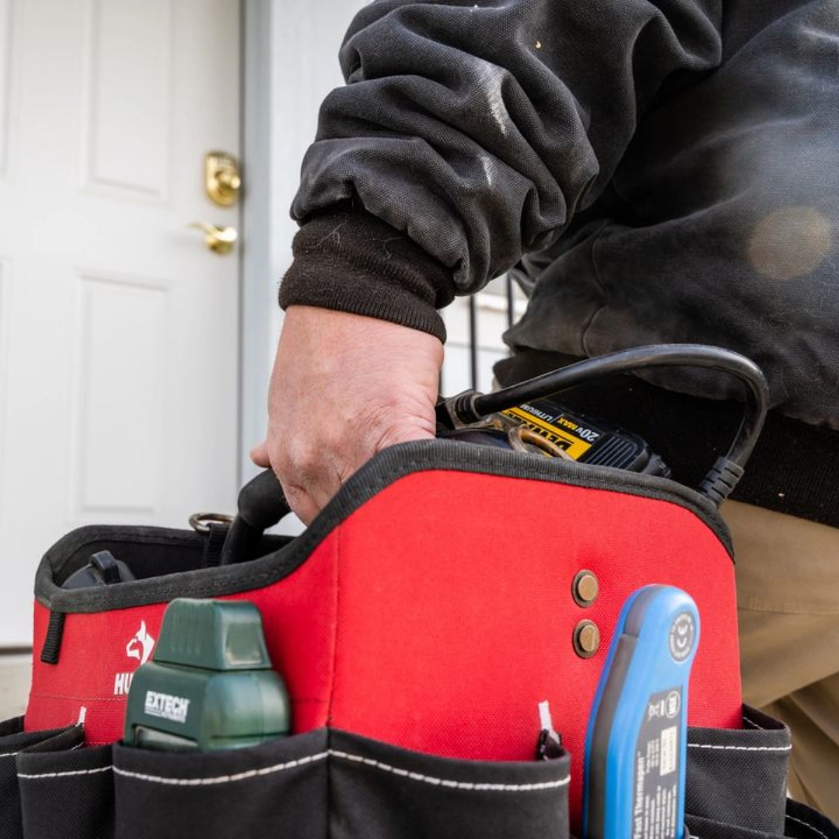 Person's hand resting on a red toolbox with tools inside, in a room with a door in the background.