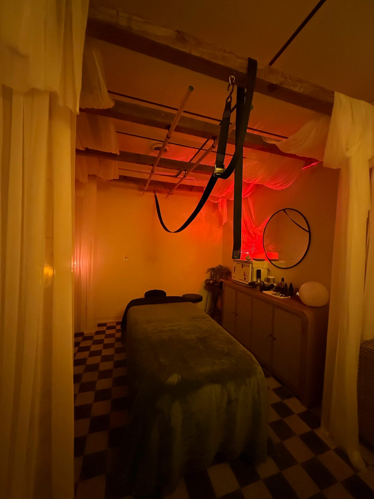 Room with bed, desk, and checkered floor, illuminated by red and warm lighting, viewed from the side.