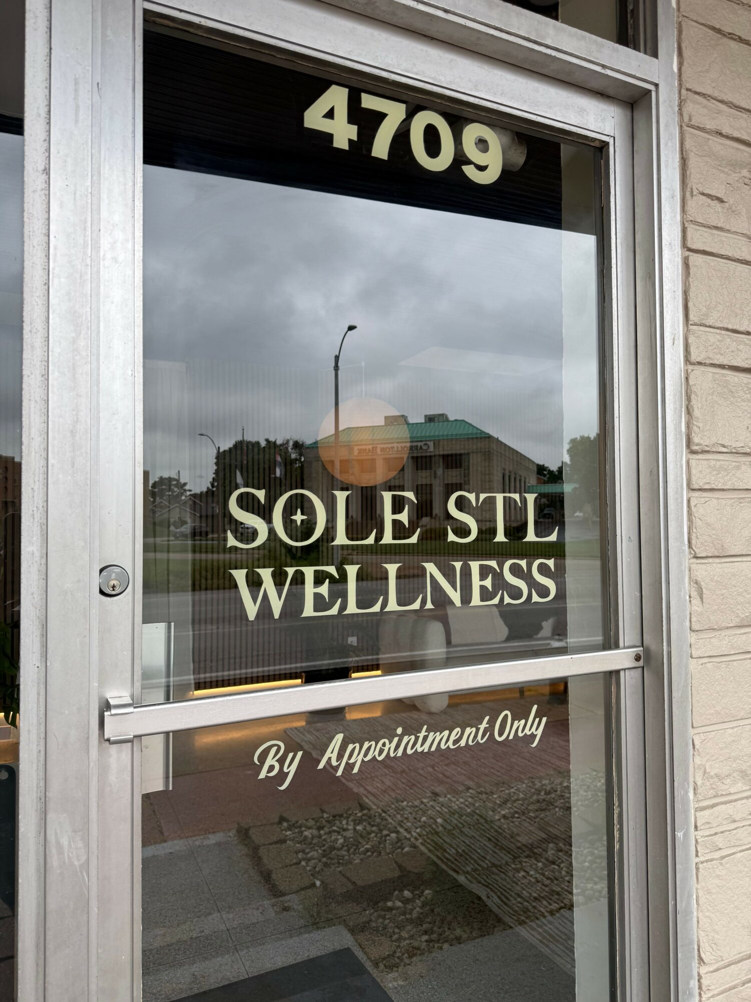 Glass door with the number 479, reflecting a building and cloudy sky, and a sign reading 'SO+L WELLNESS' with additional text.