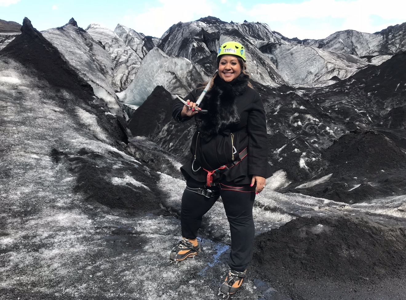 Person wearing a helmet and outdoor gear standing on rocky terrain with mountainous background.