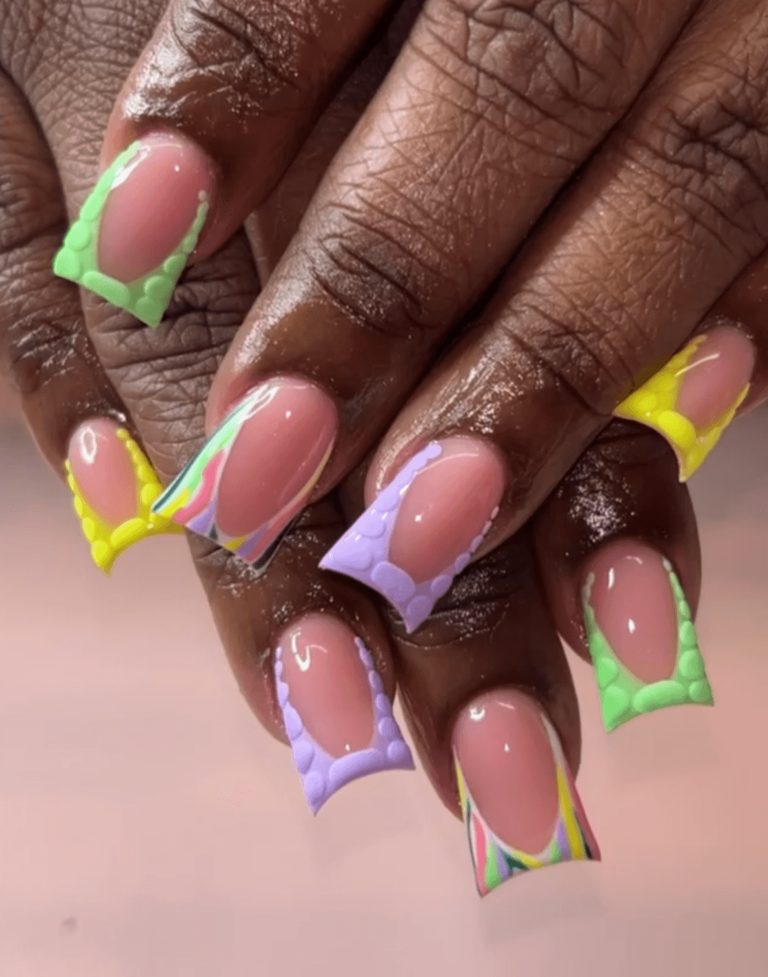 Close-up of hands with colorful, decorated nail art featuring pastel and rainbow designs, and green and yellow accents.