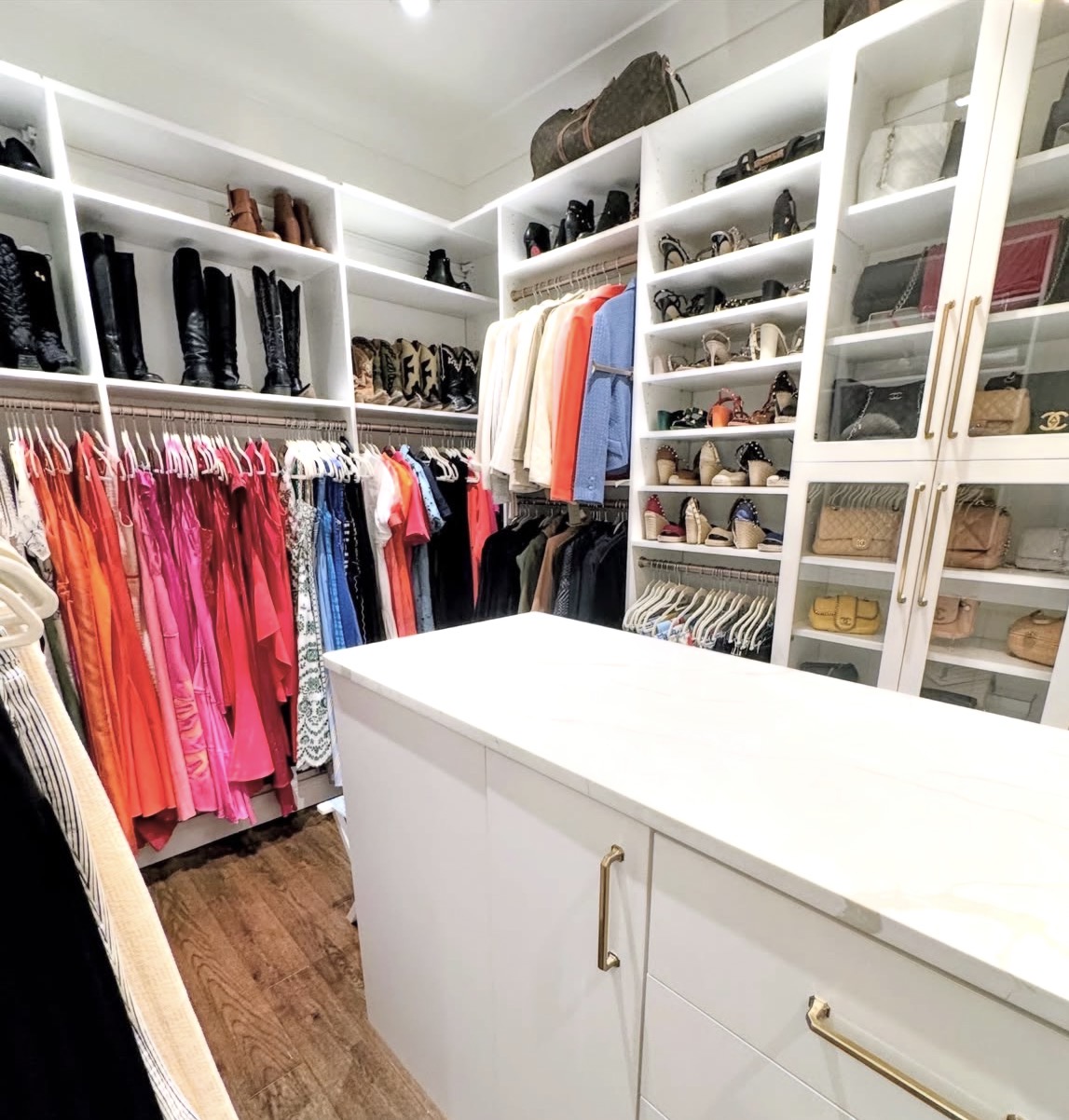 Closet with clothing, shoes, and accessories organized on shelves and hanging rods, with a white island in the center.