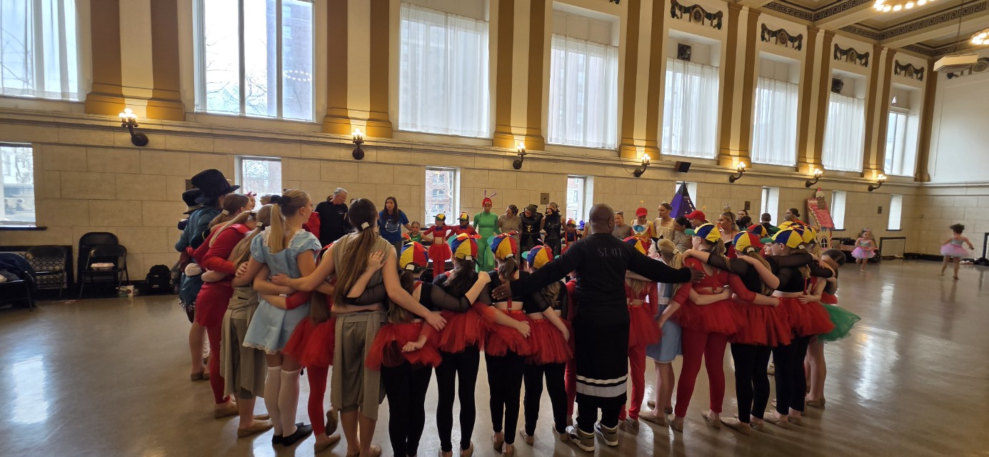 Group of children and adults in a gymnasium, standing in a circle with arms outstretched, participating in an activity.