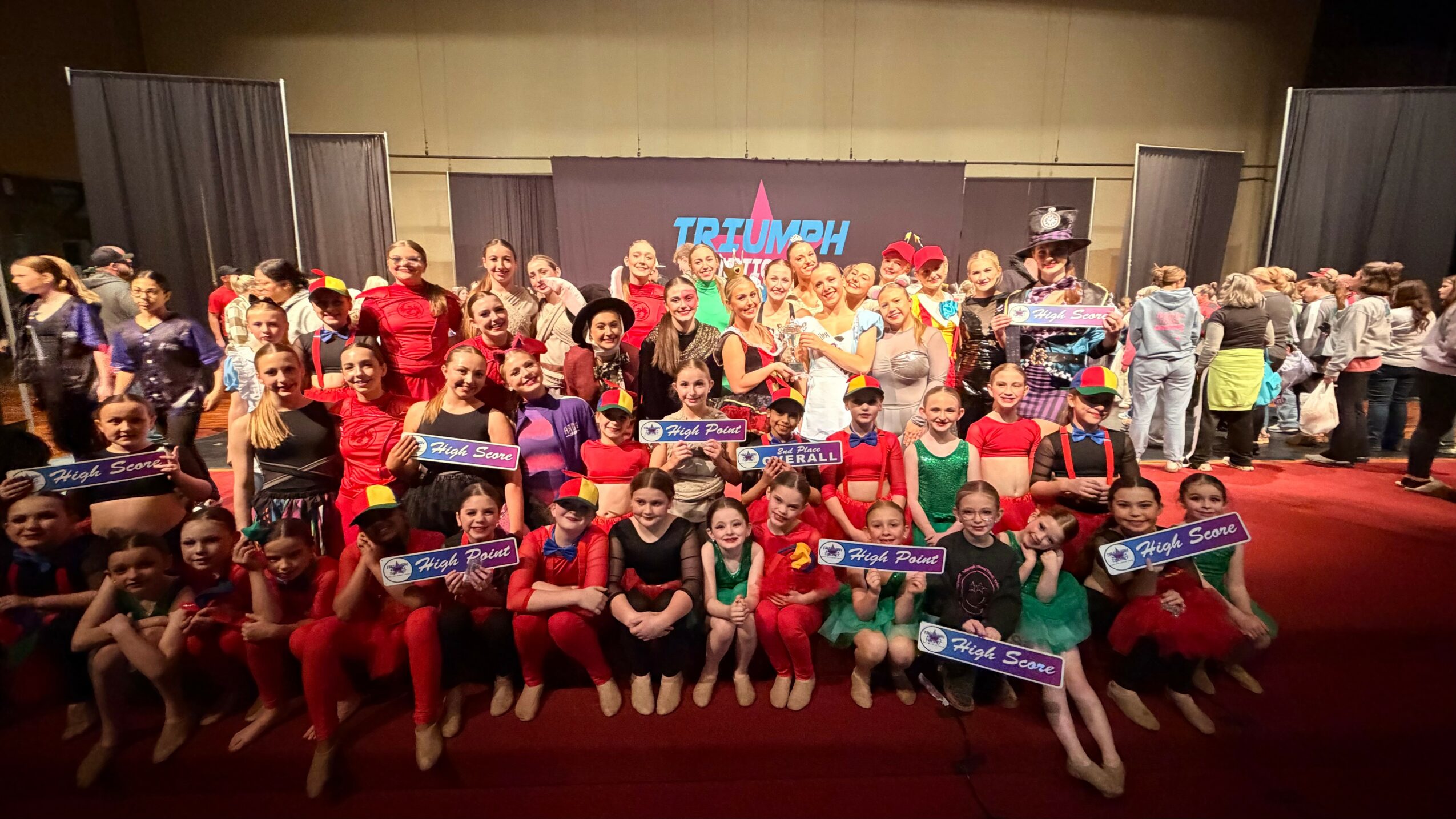 Group of children and adults posing on stage holding banners, with a TRT logo in the background.