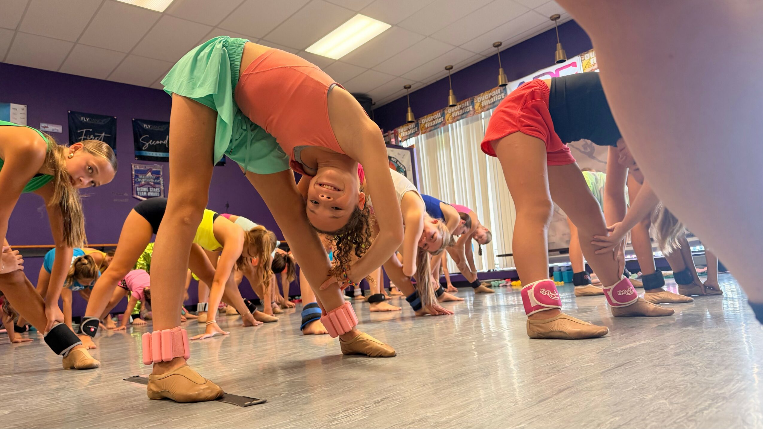 Children in colorful clothes and socks participate in a stretching exercise in a room with a wooden floor.
