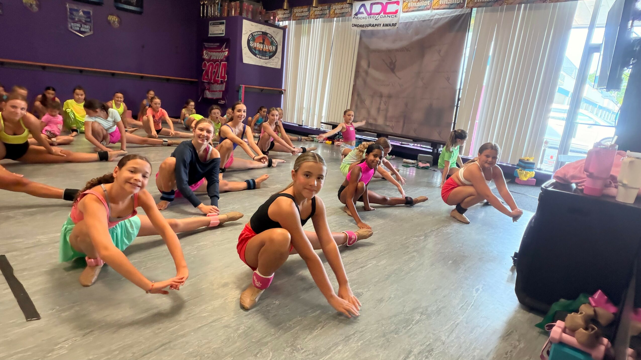 Group of children in colorful workout clothes stretching on the floor in a dance studio.