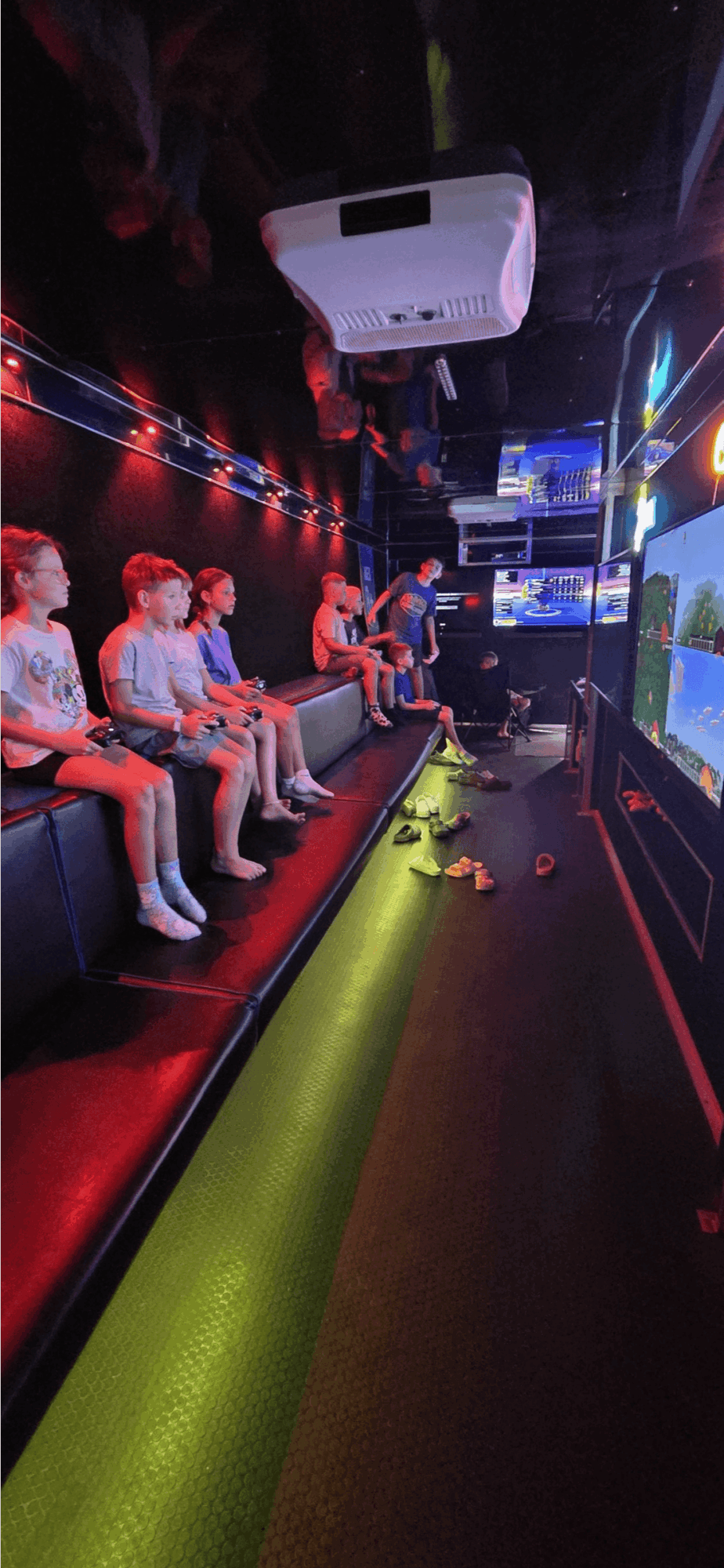 Group of children seated in a dark room watching multiple screens displaying a game or simulation.