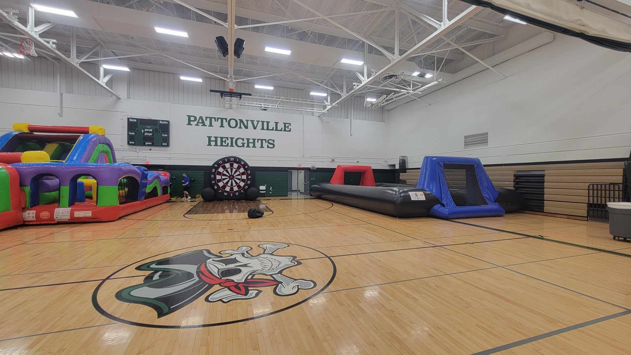 Indoor gymnasium with inflatable play structures, a dartboard, and a logo on the floor, with a sign reading 'Pattonville Heights'.