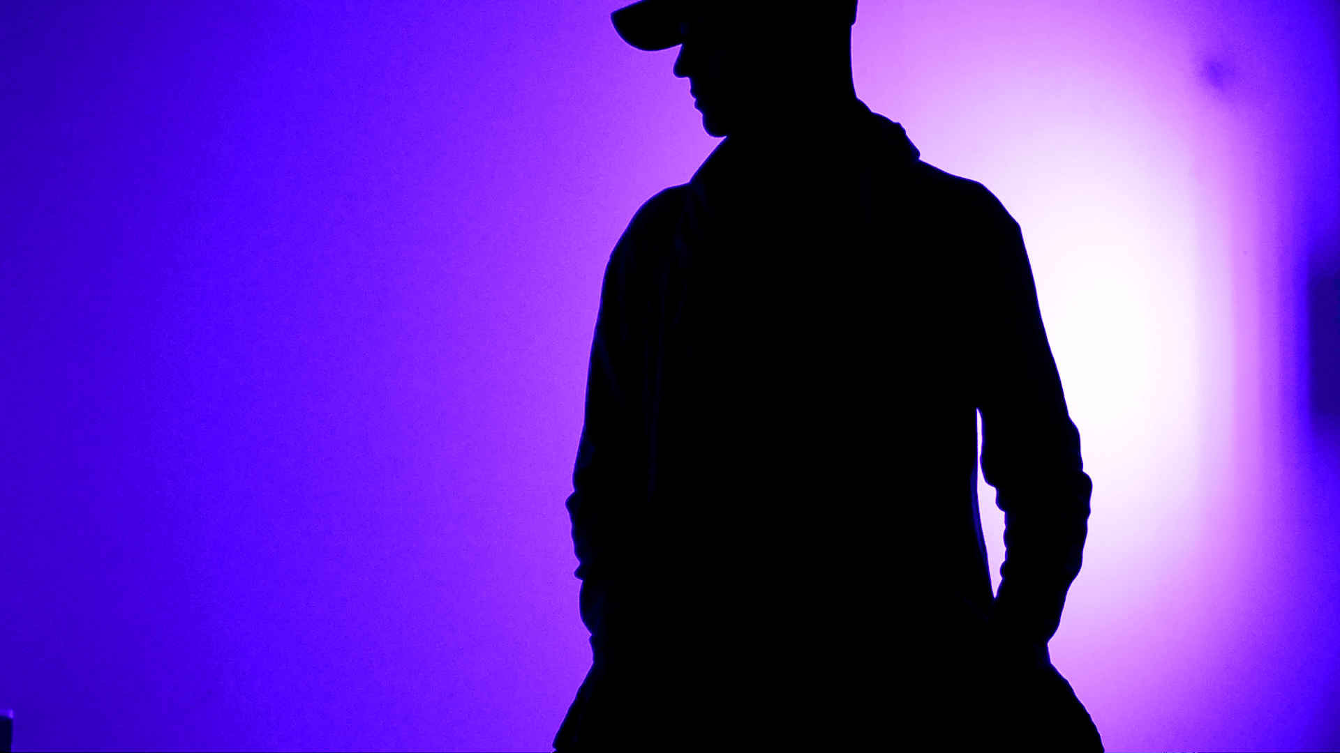 Silhouette of a person wearing a hat against a purple and blue gradient background.