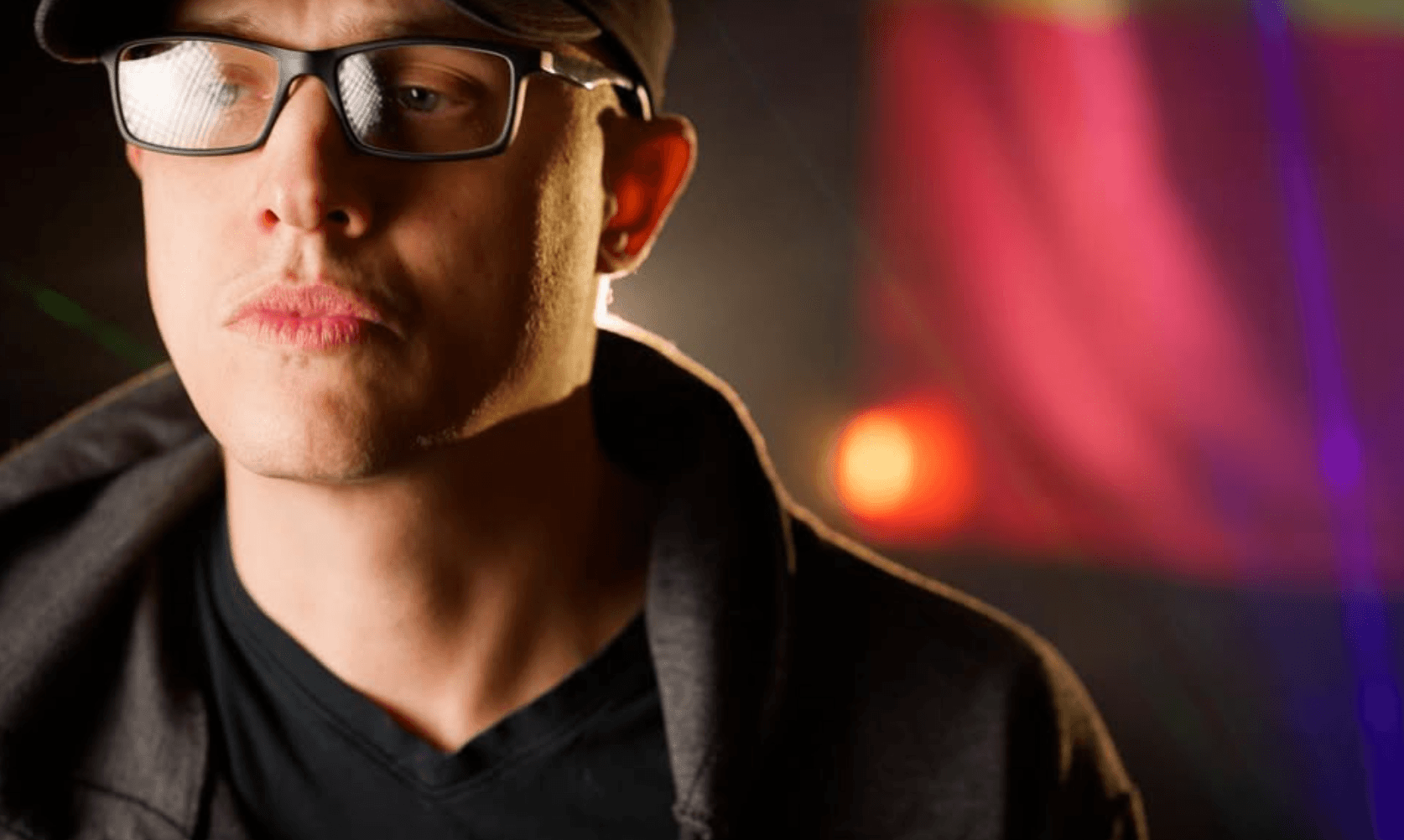 Close-up of a person wearing glasses and a hoodie, with colorful blurred background.