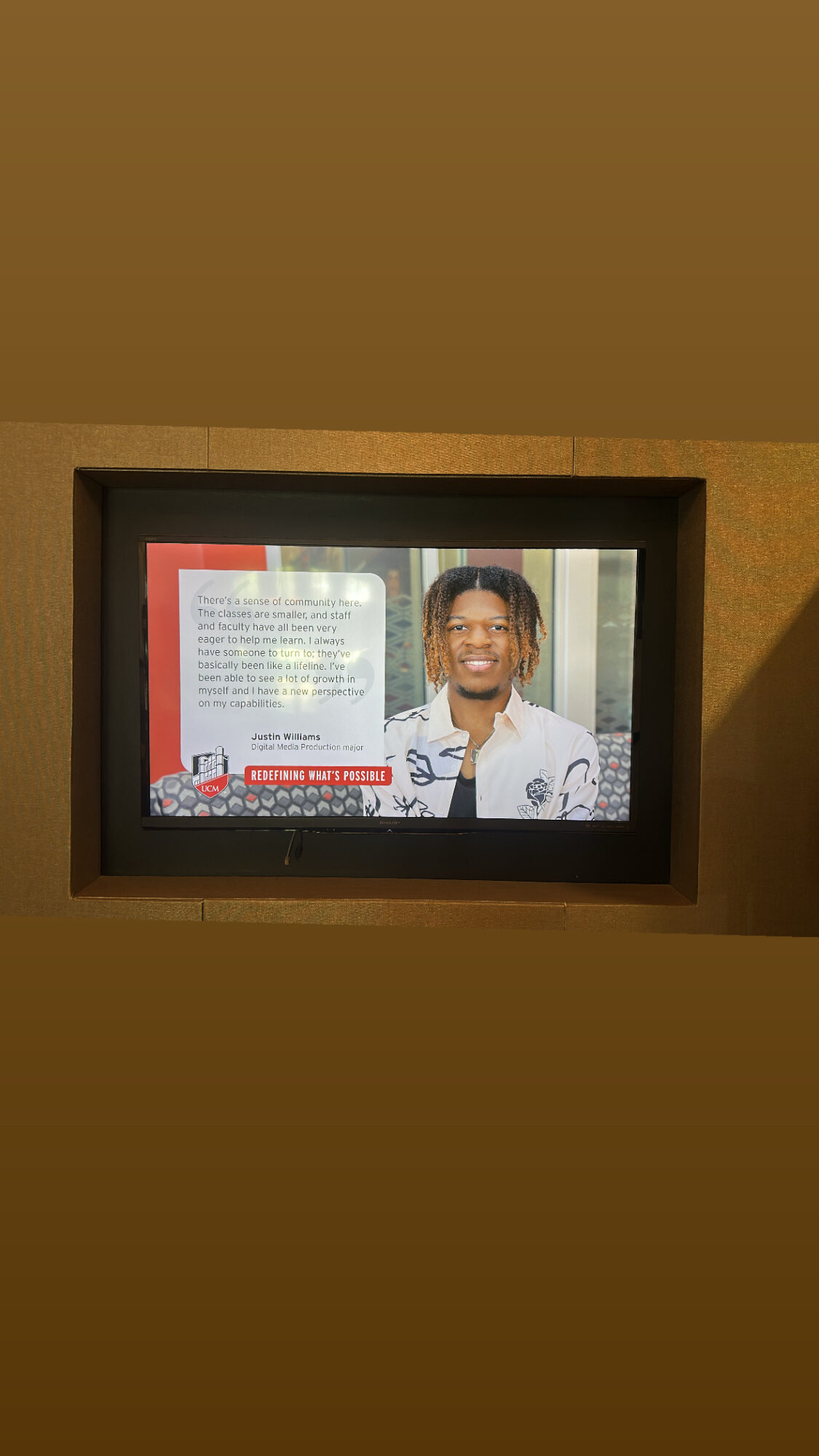 Person with short hair and glasses smiling, next to a display with text and images, in an indoor setting.