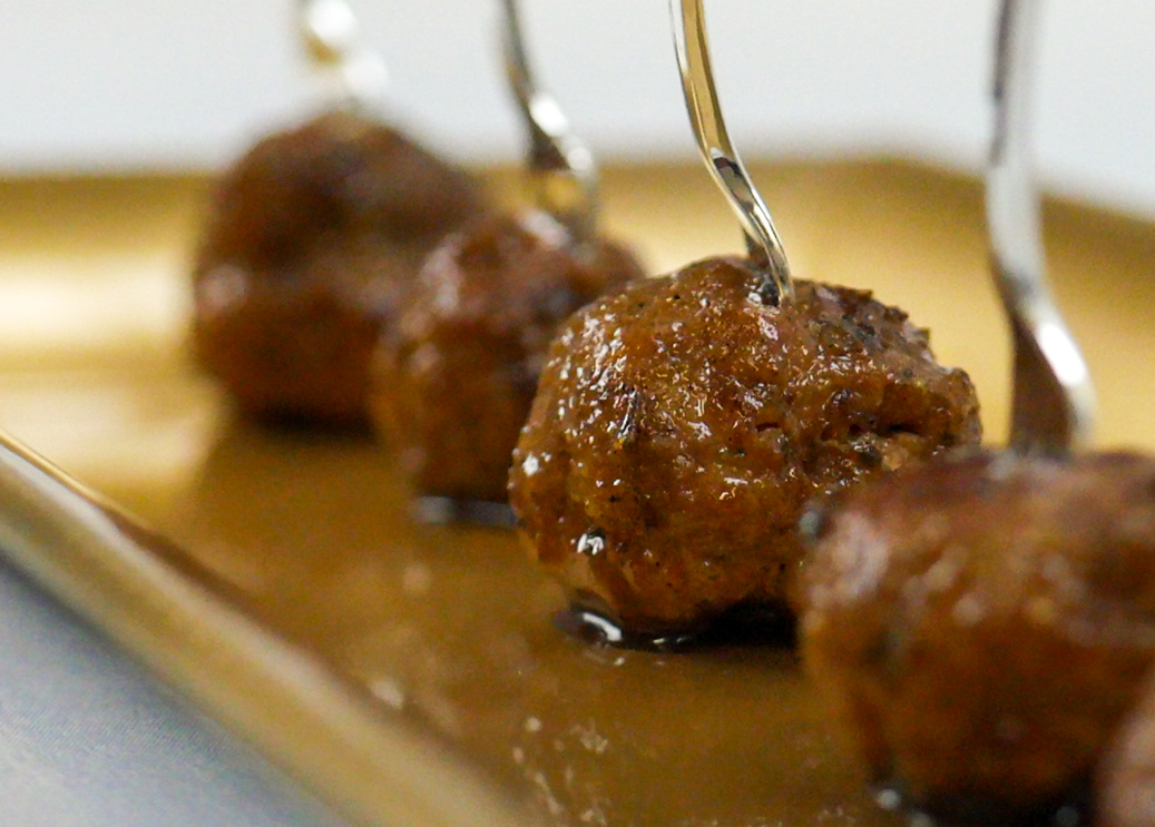 Close-up of skewered meatballs on a tray, glazed with sauce, with a blurred background.
